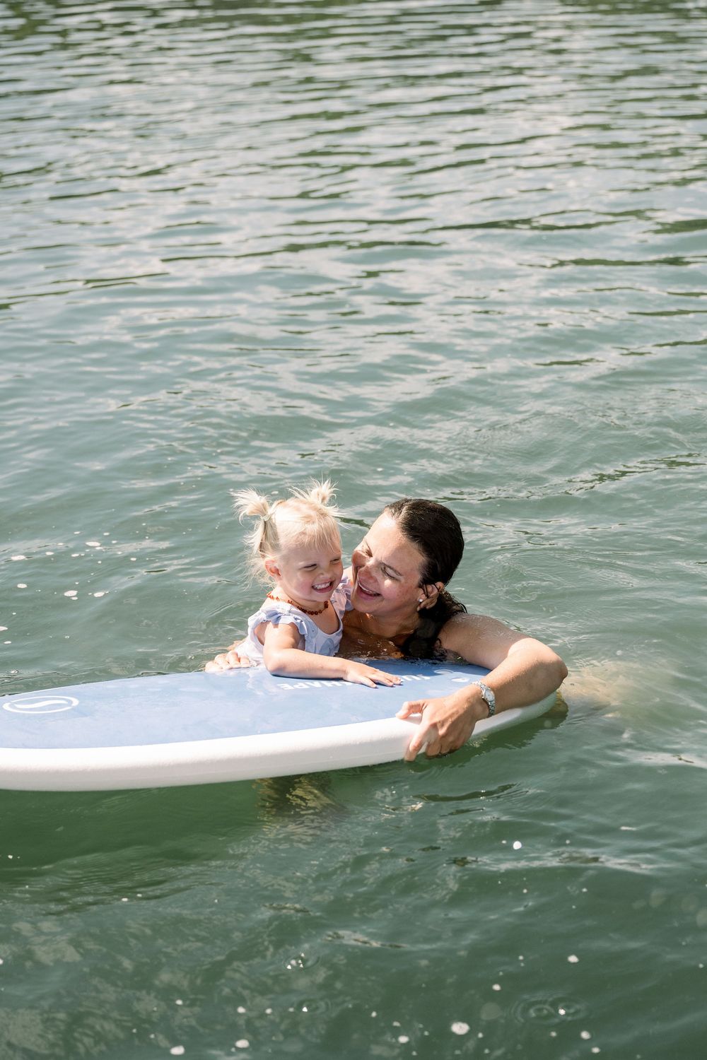 Two people enjoy swimming and floating on a paddle board in tranquil lake waters.