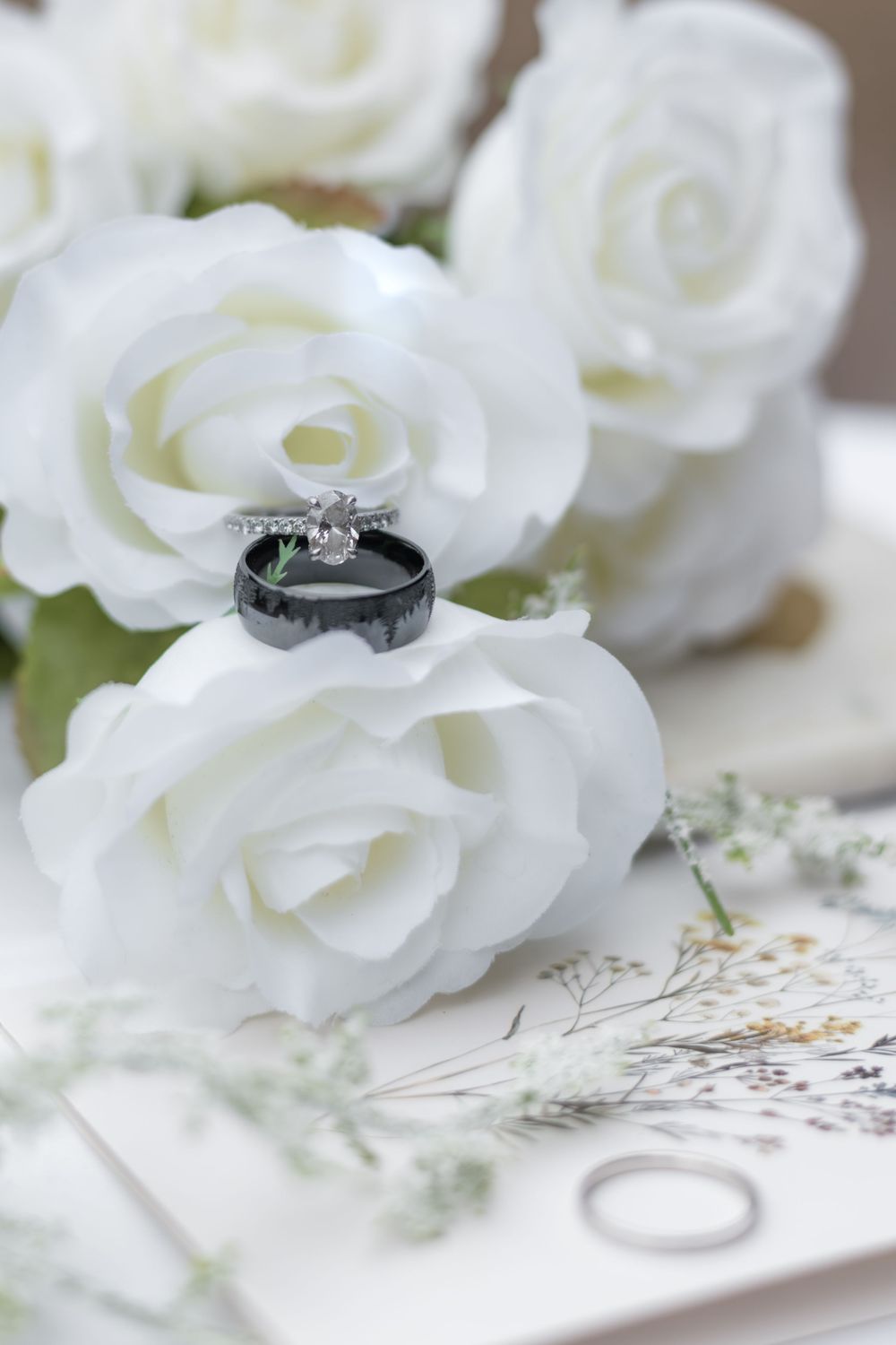 Wedding rings resting on white roses with delicate baby's breath flowers and romantic decor in soft focus.