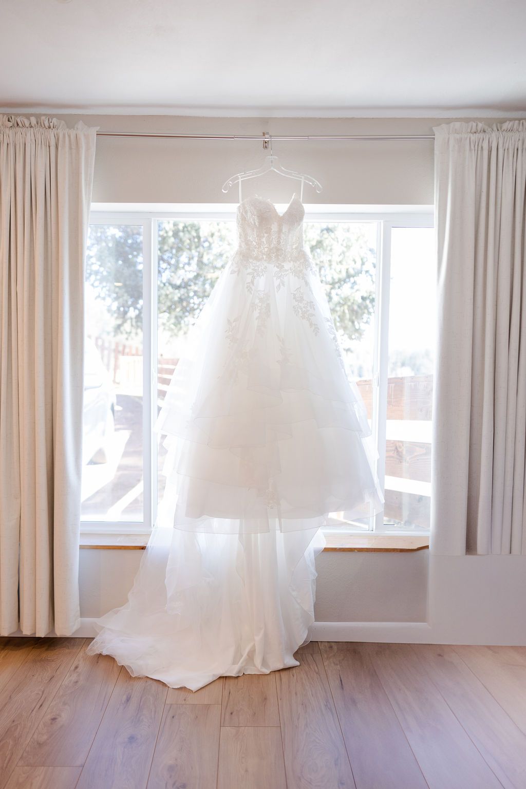 White wedding dresses hanging in a bright room with hardwood floors and natural light streaming through windows.