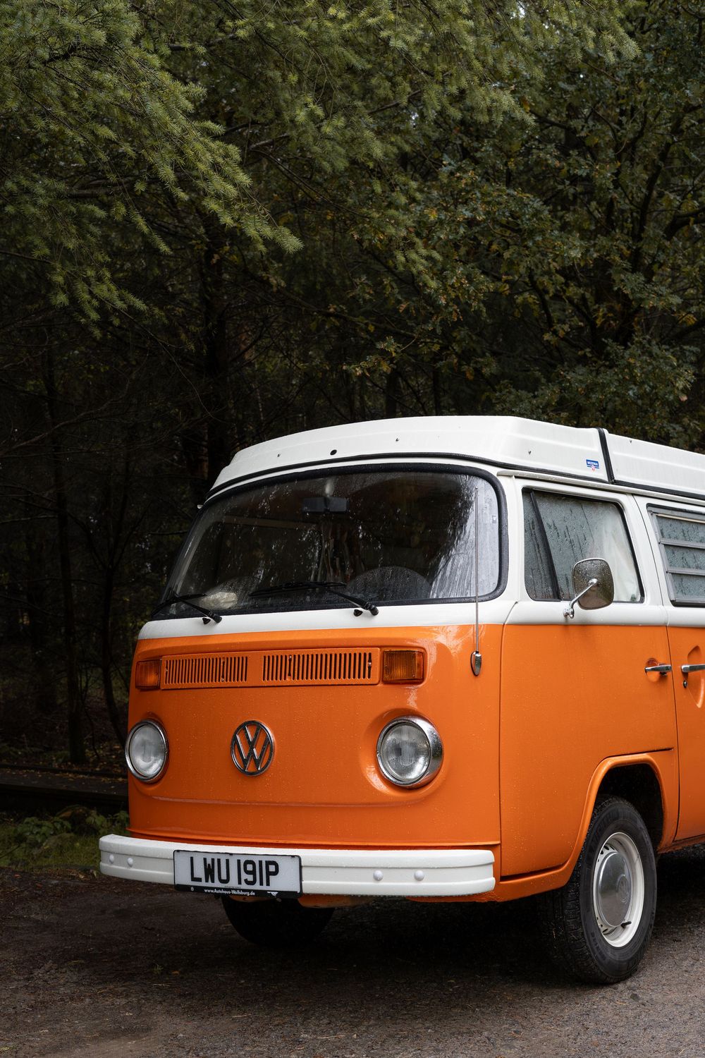 Classic orange and white Volkswagen Type 2 van photographed in a wooded setting from multiple angles.