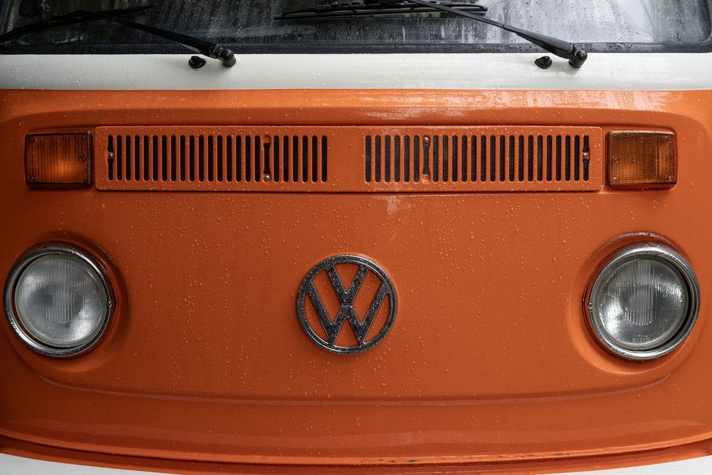 Close-up details of a vintage orange Volkswagen van showing headlights, grill, and VW emblem.