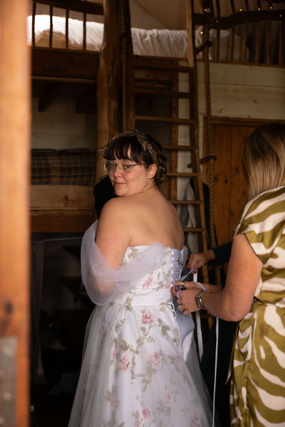 A person wearing a white floral dress stands in a rustic barn-like setting with wooden beams and posts.