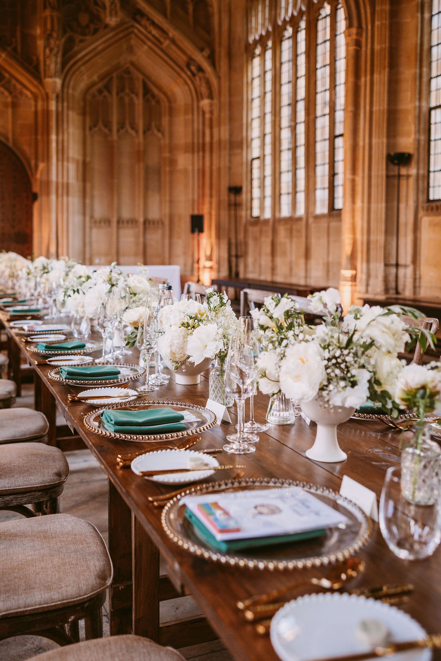 Elegant wedding reception table setting with turquoise chargers, white floral centerpieces and gothic cathedral windows.