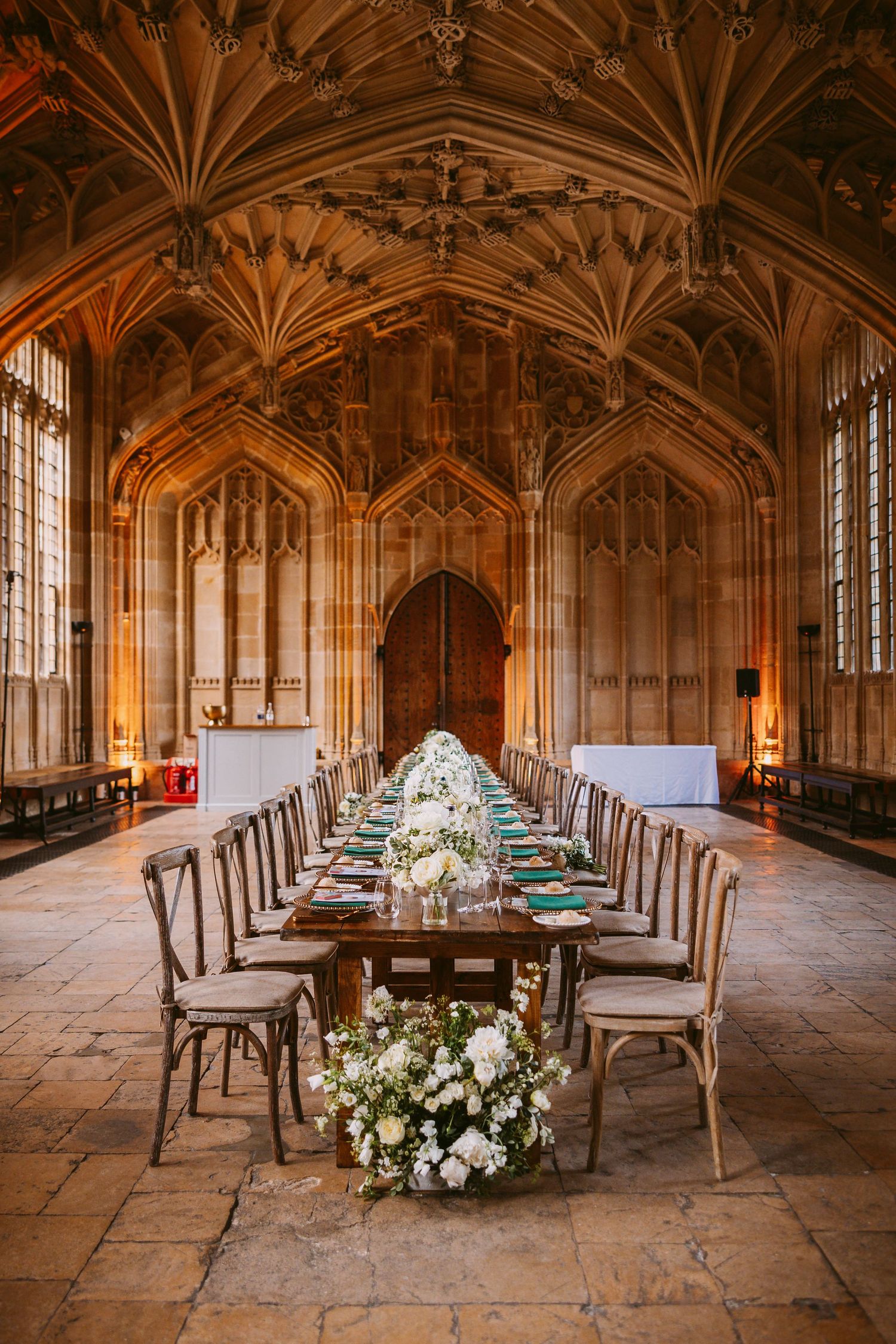 Gothic stone dining hall with vaulted ceiling and elegant floral centerpieces set for a formal event at Oxford University.