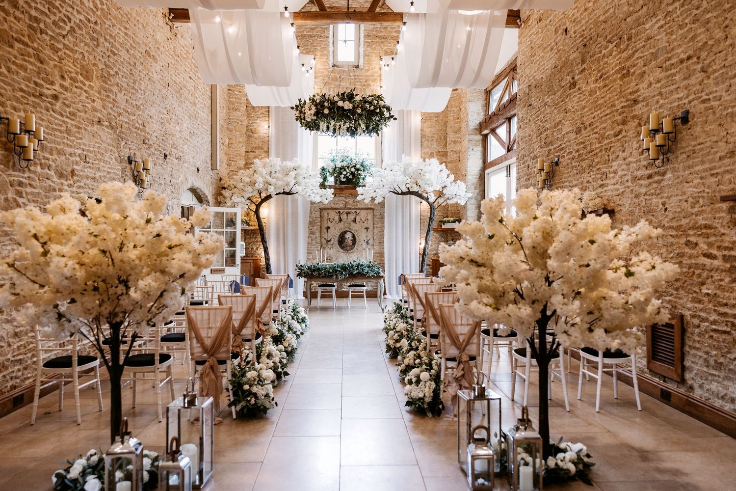 Elegant rustic wedding venue with exposed brick walls, crystal chandeliers, and white floral arrangements creating a romantic atmosphere.