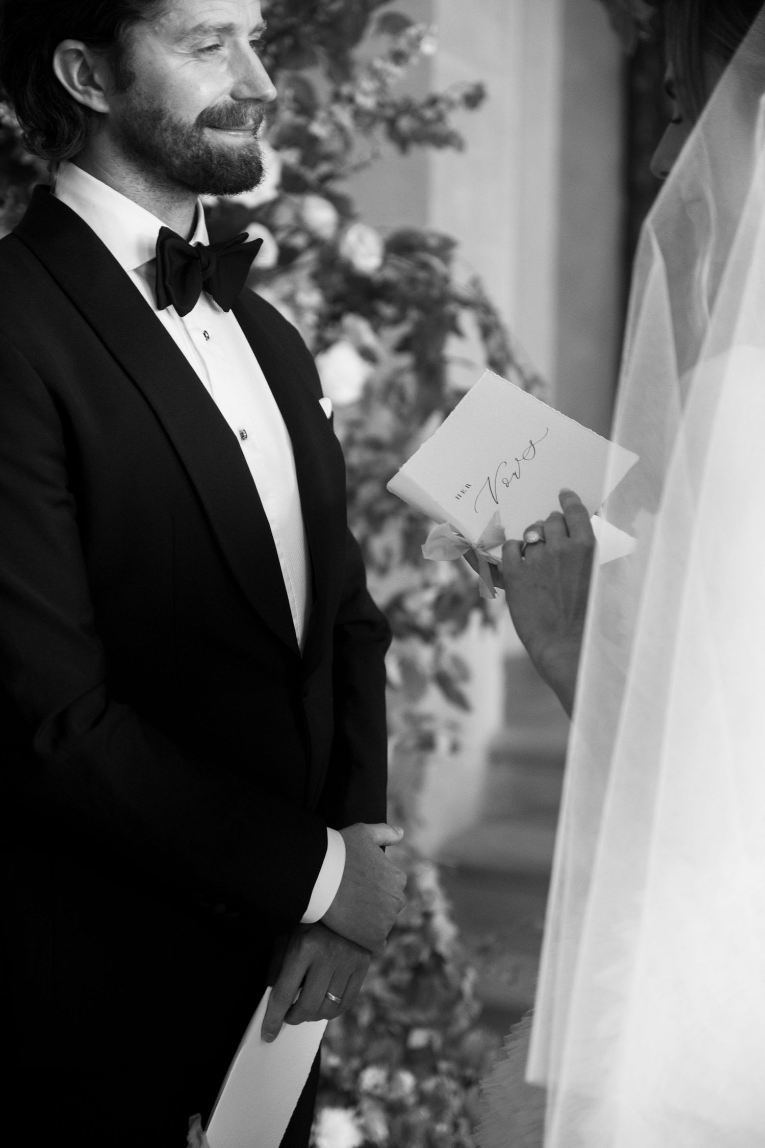 Close-up candid wedding moment showing the groom's profile in a classic black tuxedo and bow tie.
