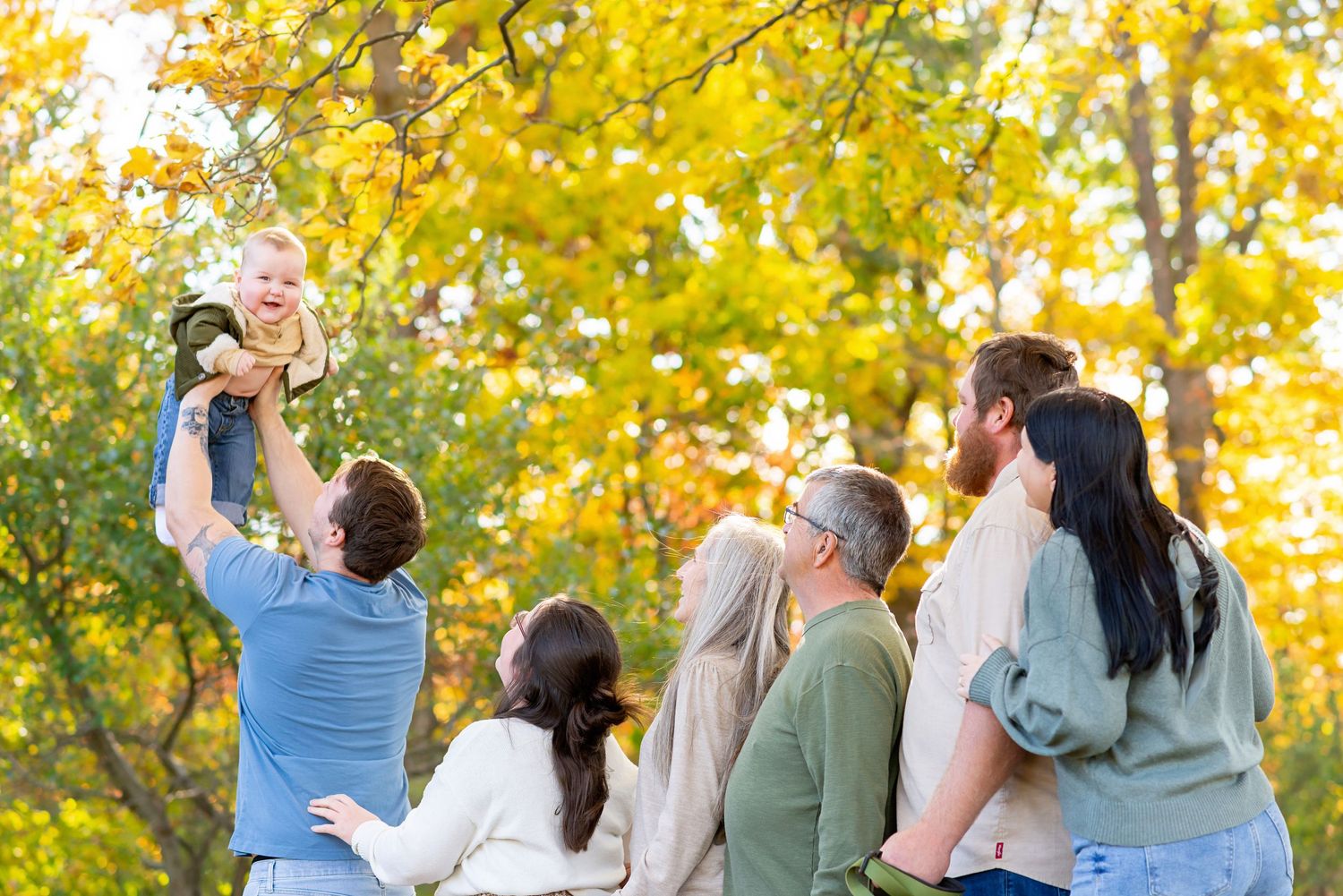 Family playing and lifting the baby of the family celebrating outdoors against golden autumn foliage at ReForest London.
