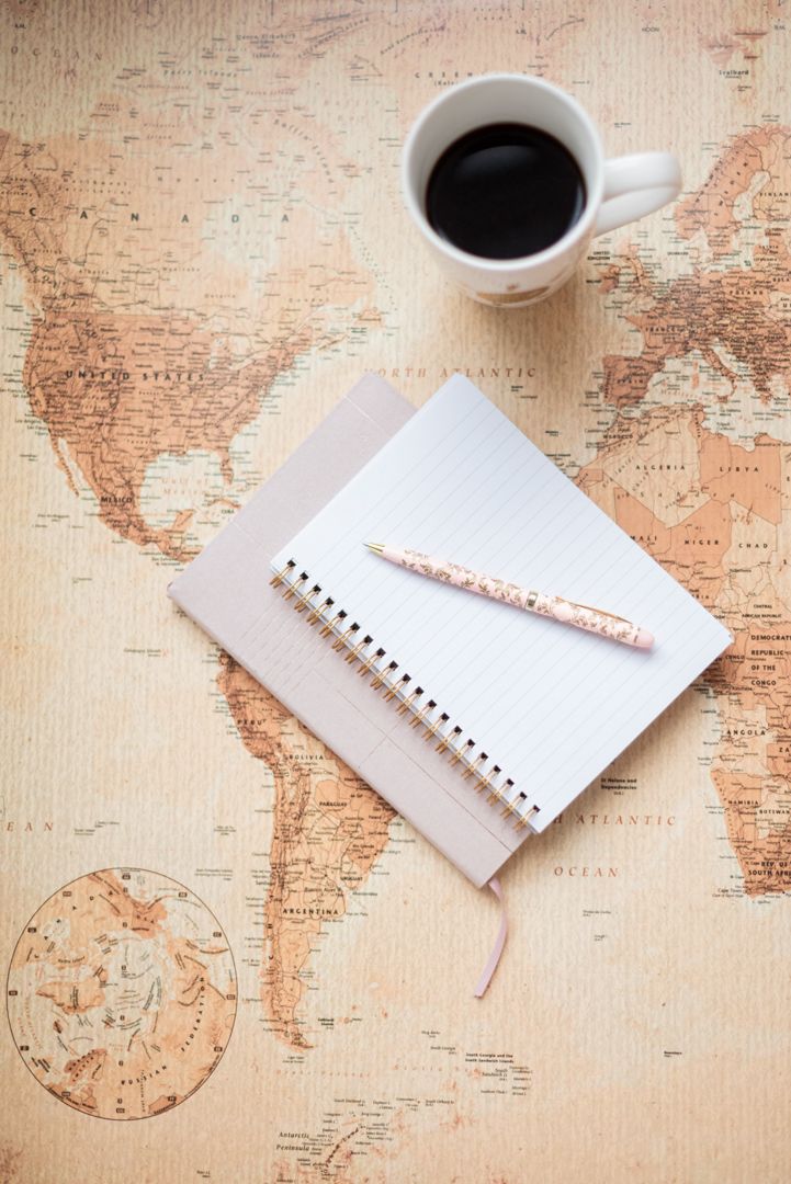 Vintage world map flatlay with coffee cup, notebook and pen creating a travel planning scene.