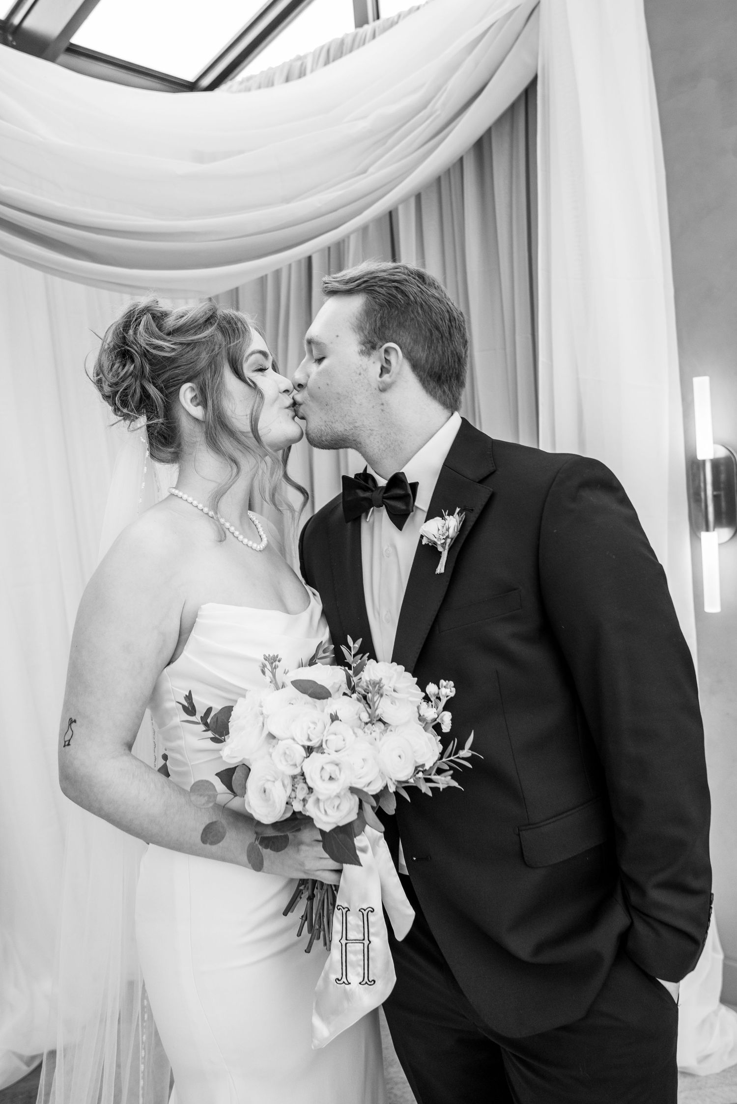 An elegant wedding moment captured in front of white drapery and soft lighting.