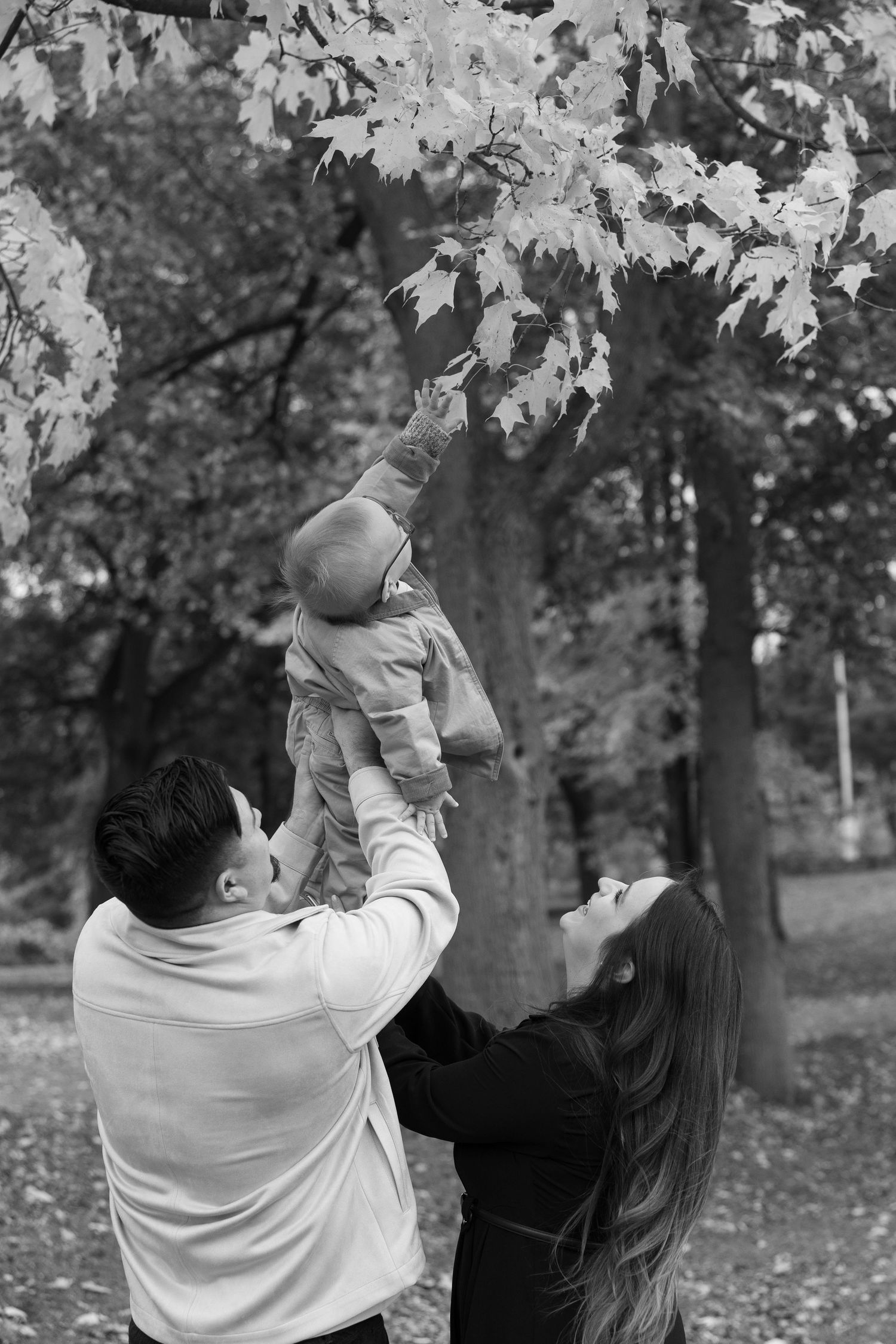 Black and white sequence of a parent playfully lifting a small child in the air among autumn trees.