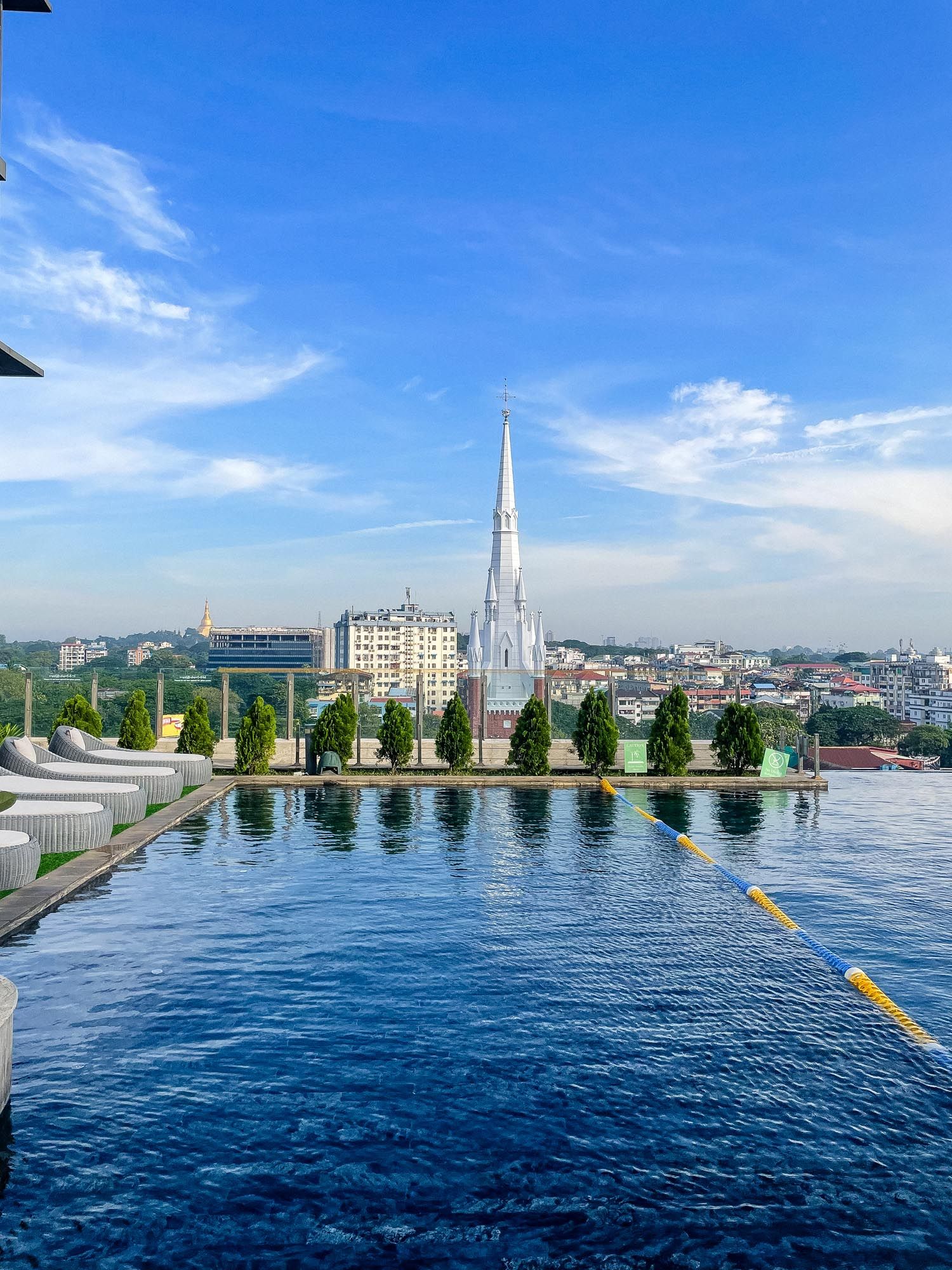 Panoramic cityscape view across blue harbor waters with modern buildings and a church spire against bright sky.