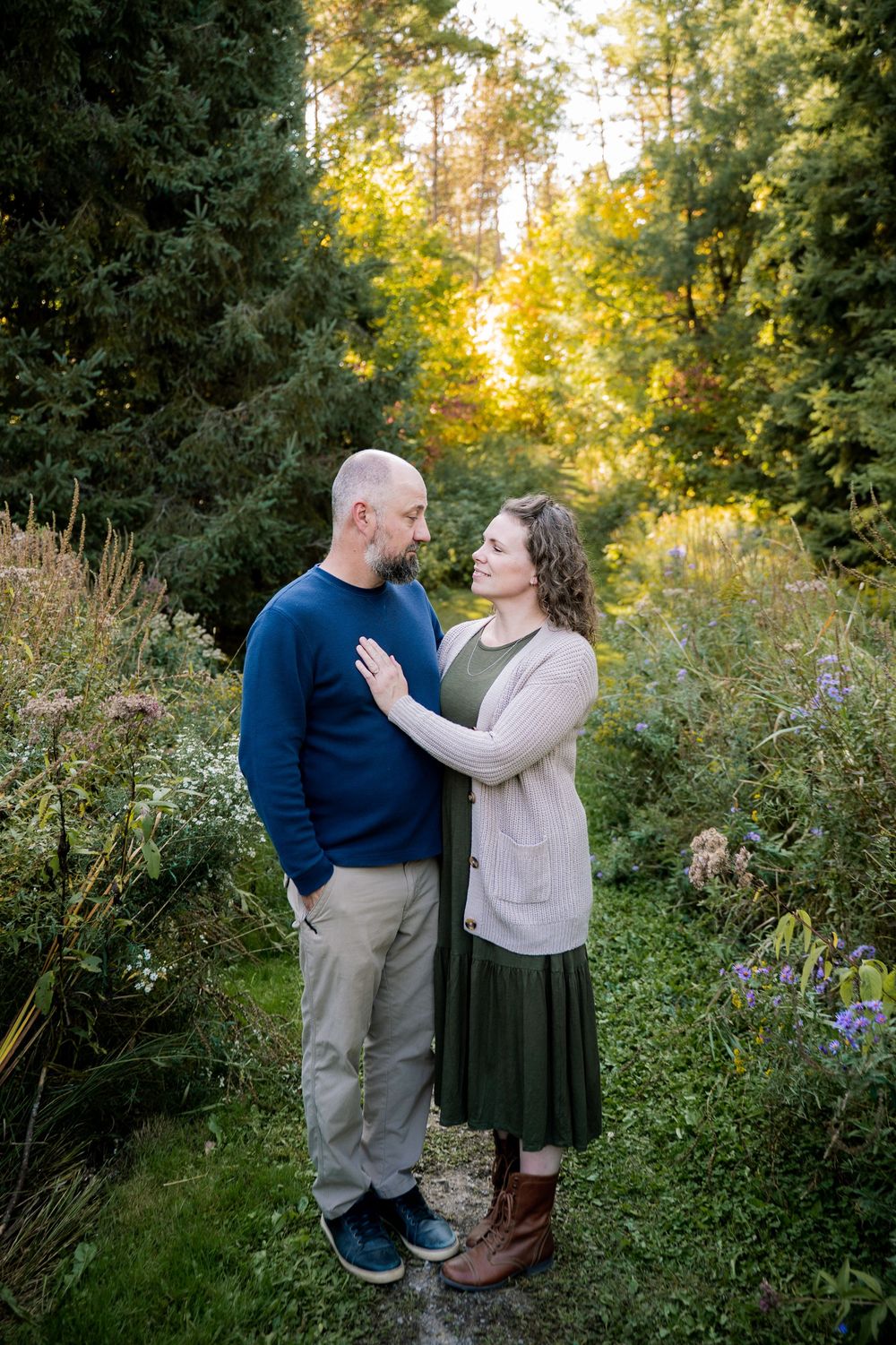 A couple shares a tender moment among wildflowers and trees during golden hour in a natural outdoor setting.