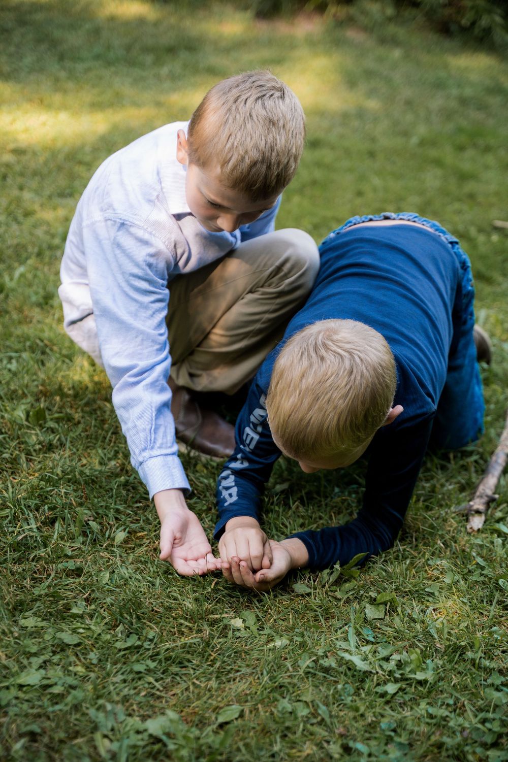 Two children in casual clothing examine something interesting in the grass on a sunny day.