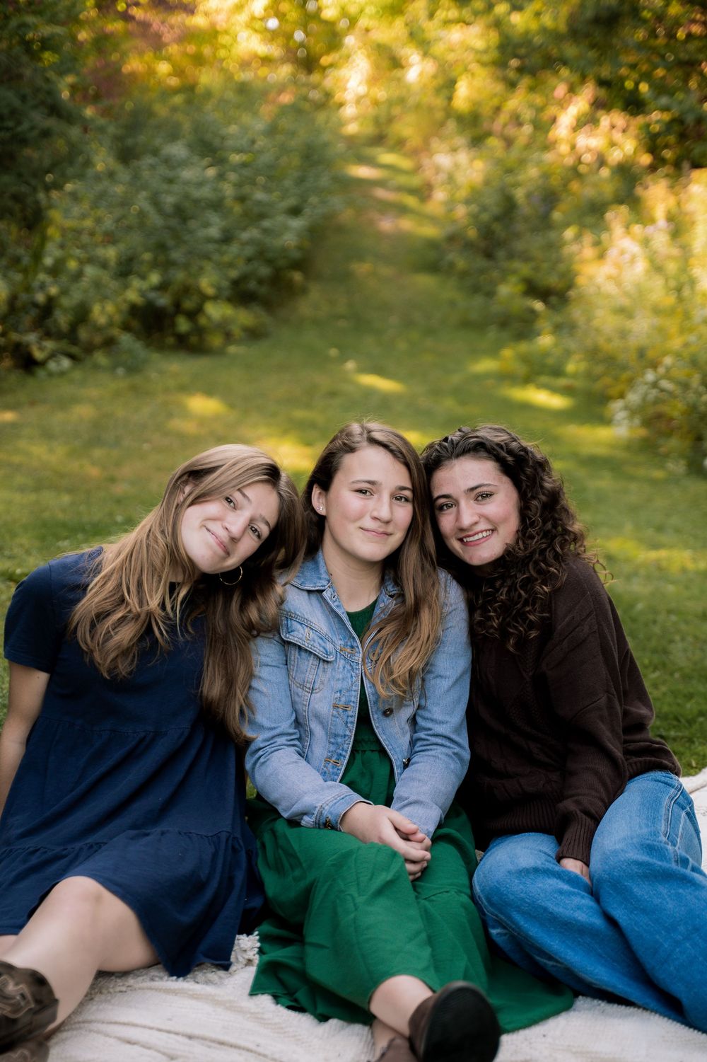 Three friends lounging together on grass during golden hour in a casual outdoor photoshoot.