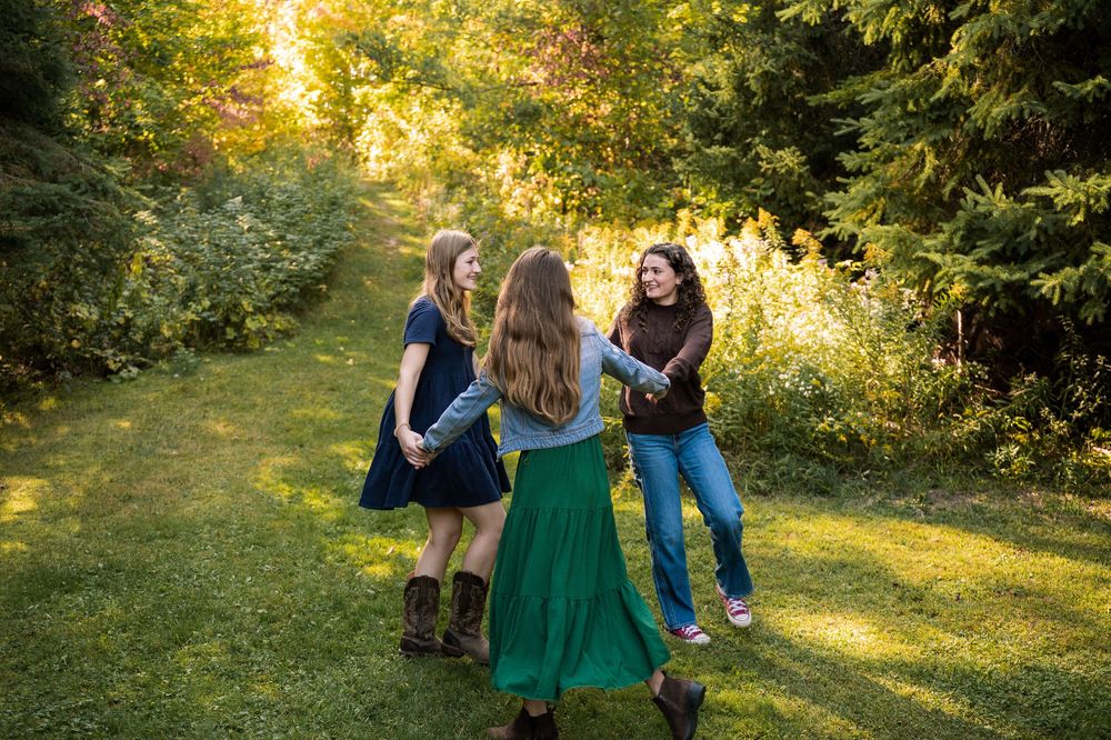 A group of people dance together in a sunlit garden with autumn foliage in the background.