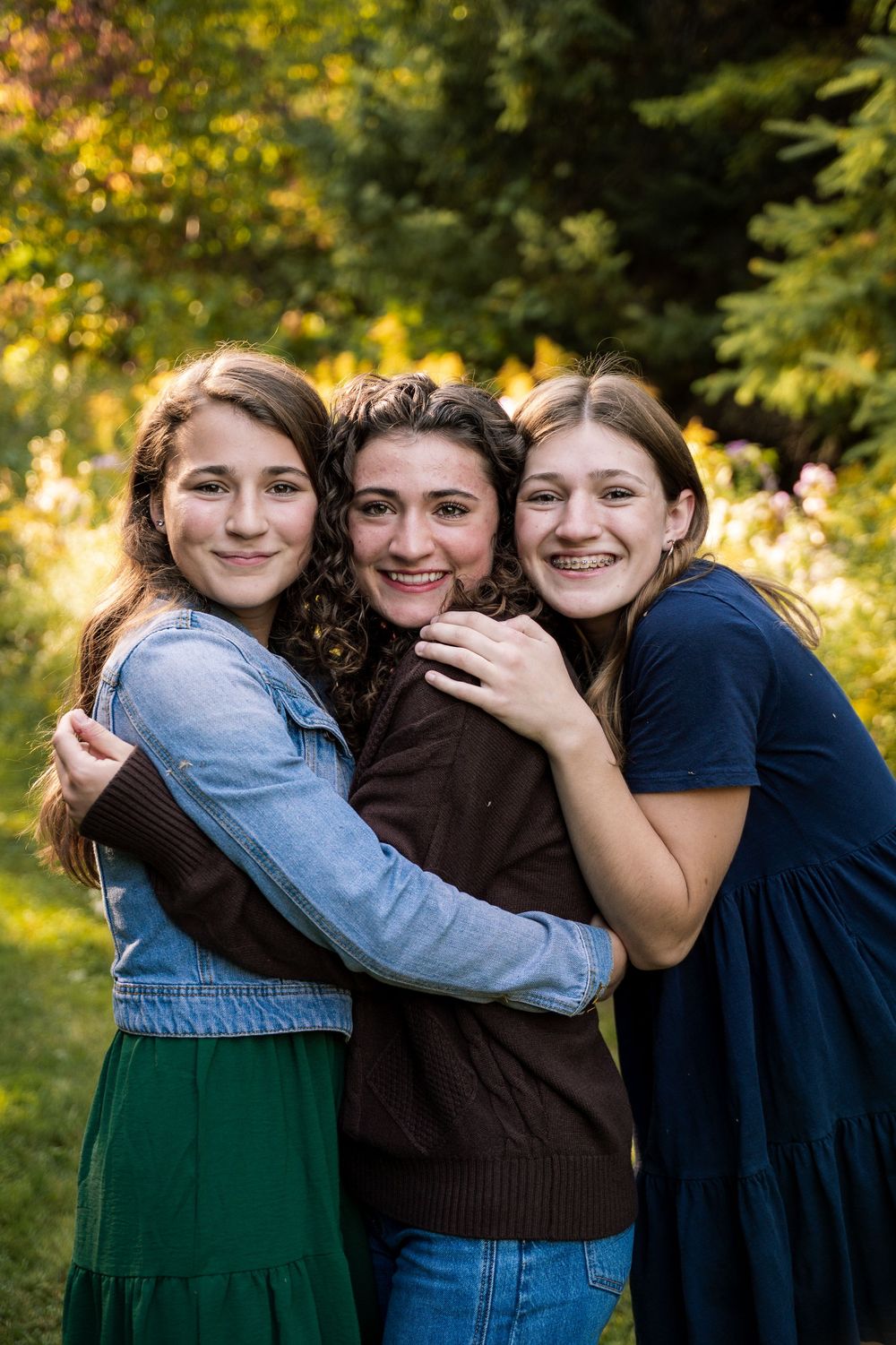A group embraces and laughs together outdoors against an autumn backdrop with golden sunlight.