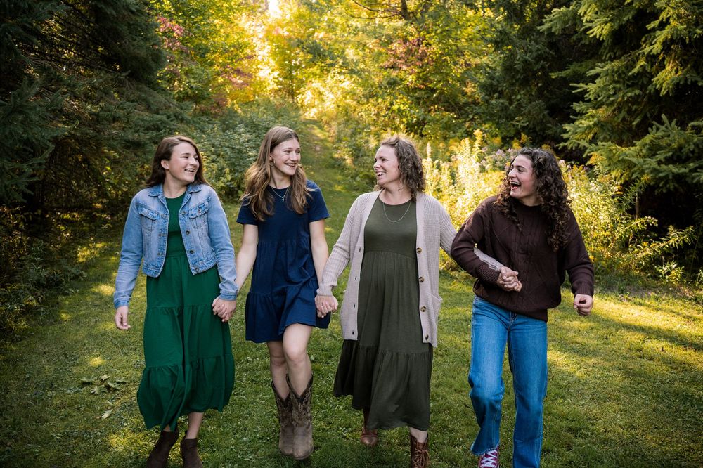 A group of friends laugh and walk together through a sunlit forest path during golden hour.