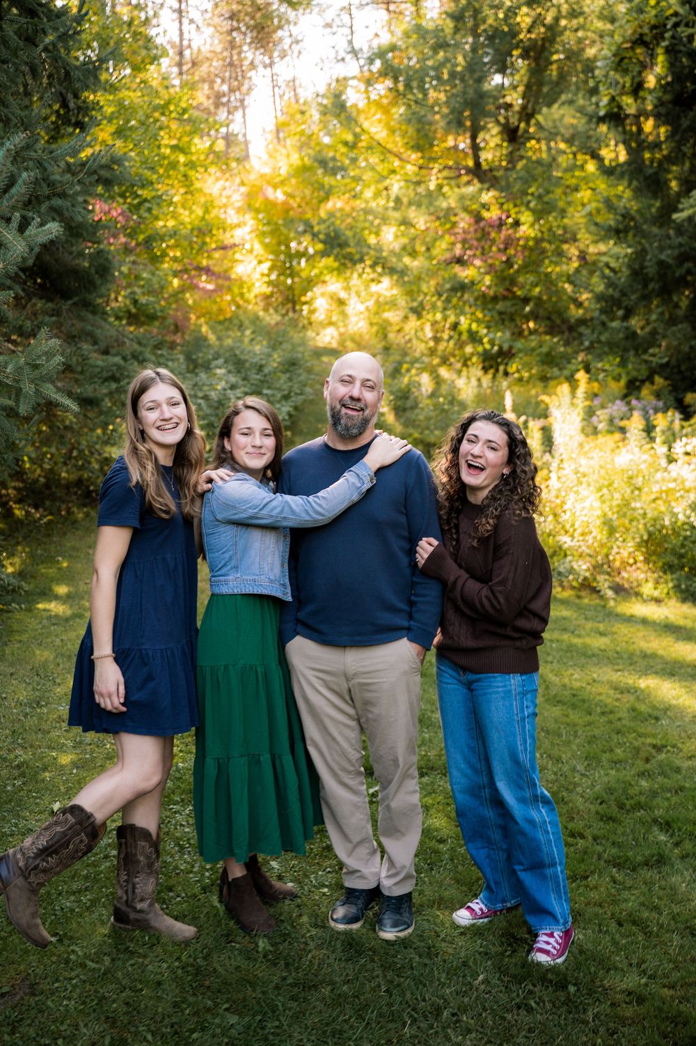 A group of friends laugh and embrace while posing together on a grassy hill during sunset.