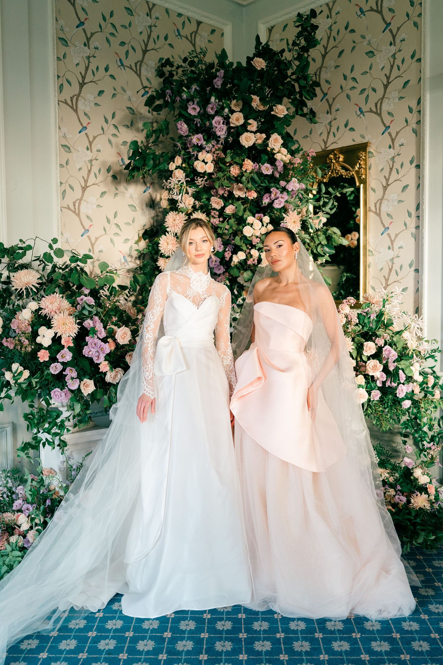 Two elegant wedding gowns, one white and one blush pink, displayed against a floral backdrop with climbing roses.
