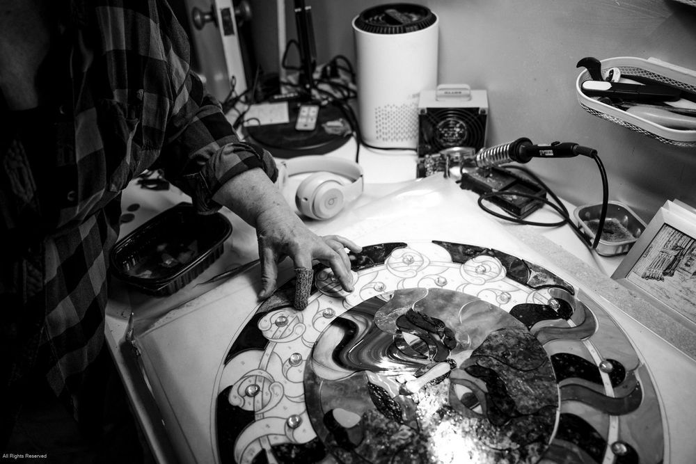 Black and white photo showing hands working on a turntable or record player with various equipment on a desk.