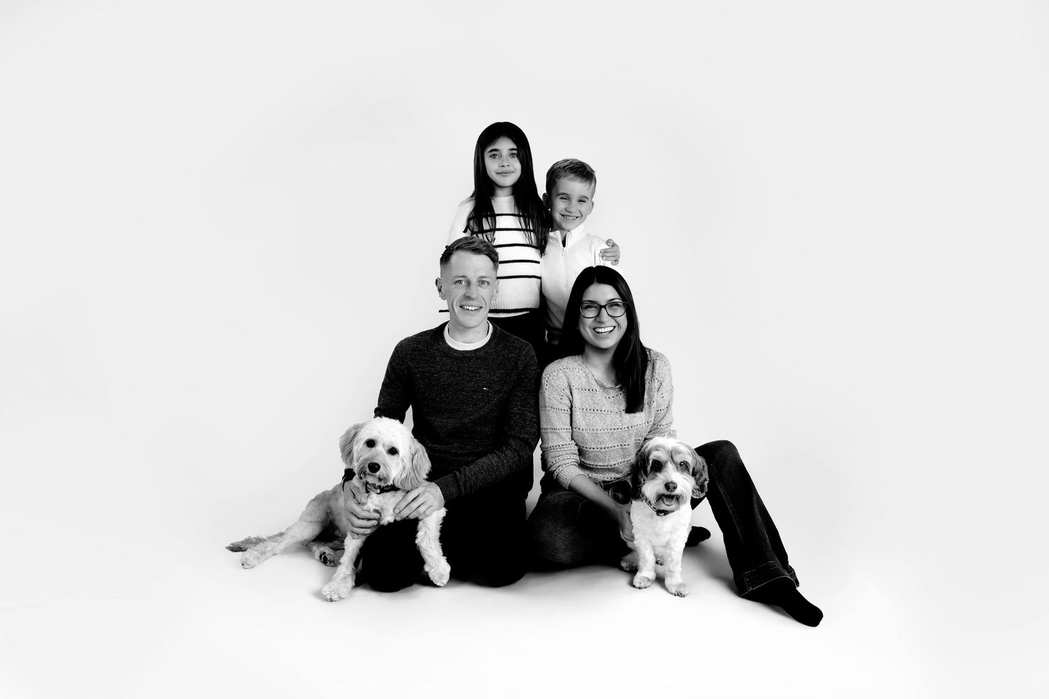 A series of black and white family portraits with a white dog sitting with people in casual attire on a light background.