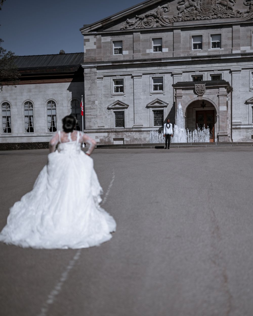 A long white wedding dress flows across the stone courtyard of a historic building.