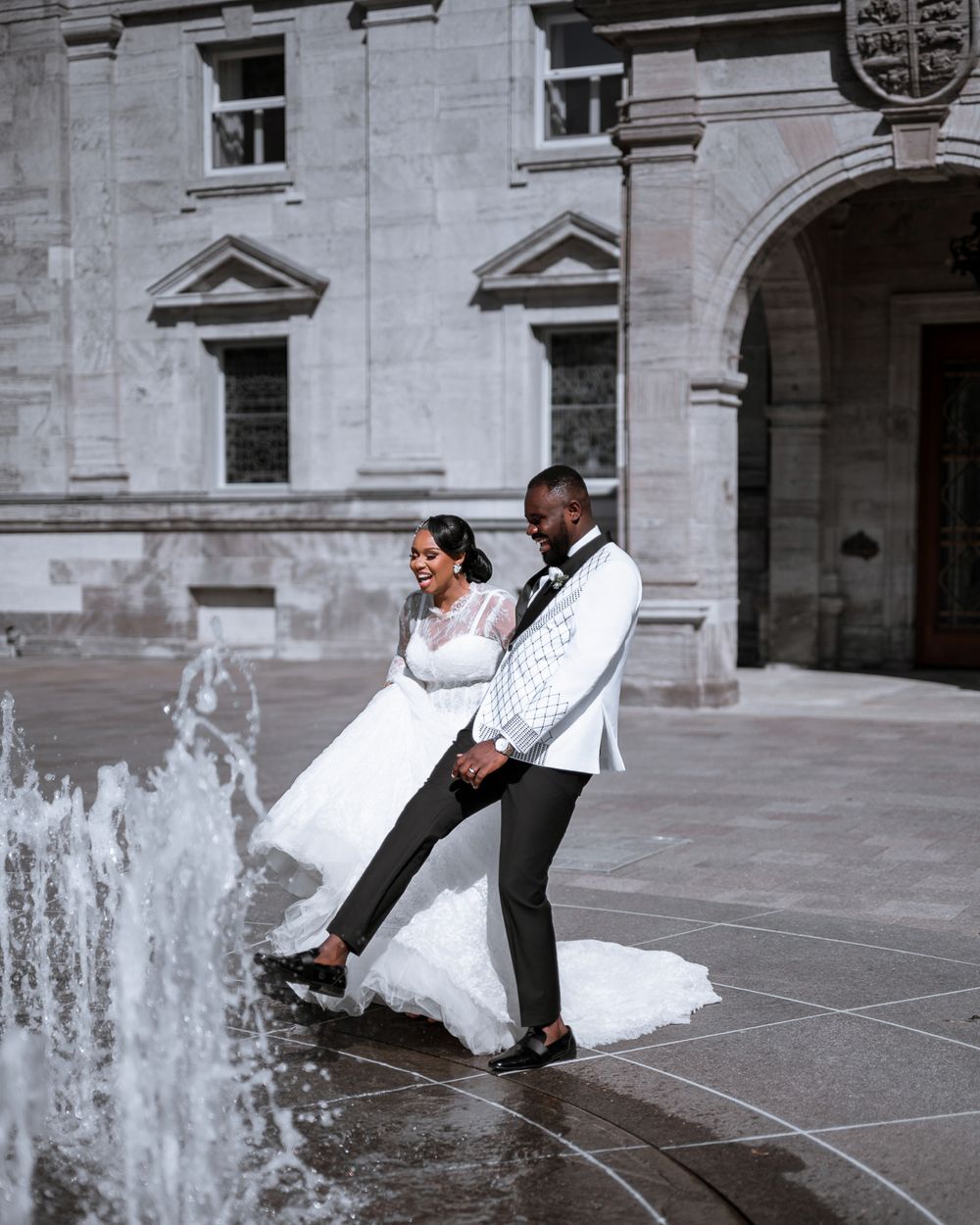A couple posing together at a grand stone building with fountains in a romantic photo sequence.