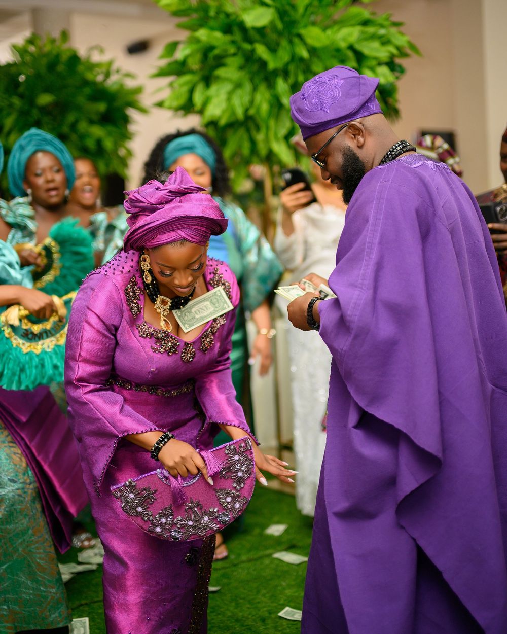 Traditional wedding guests dance and celebrate in purple and fuchsia attire at an outdoor celebration event.