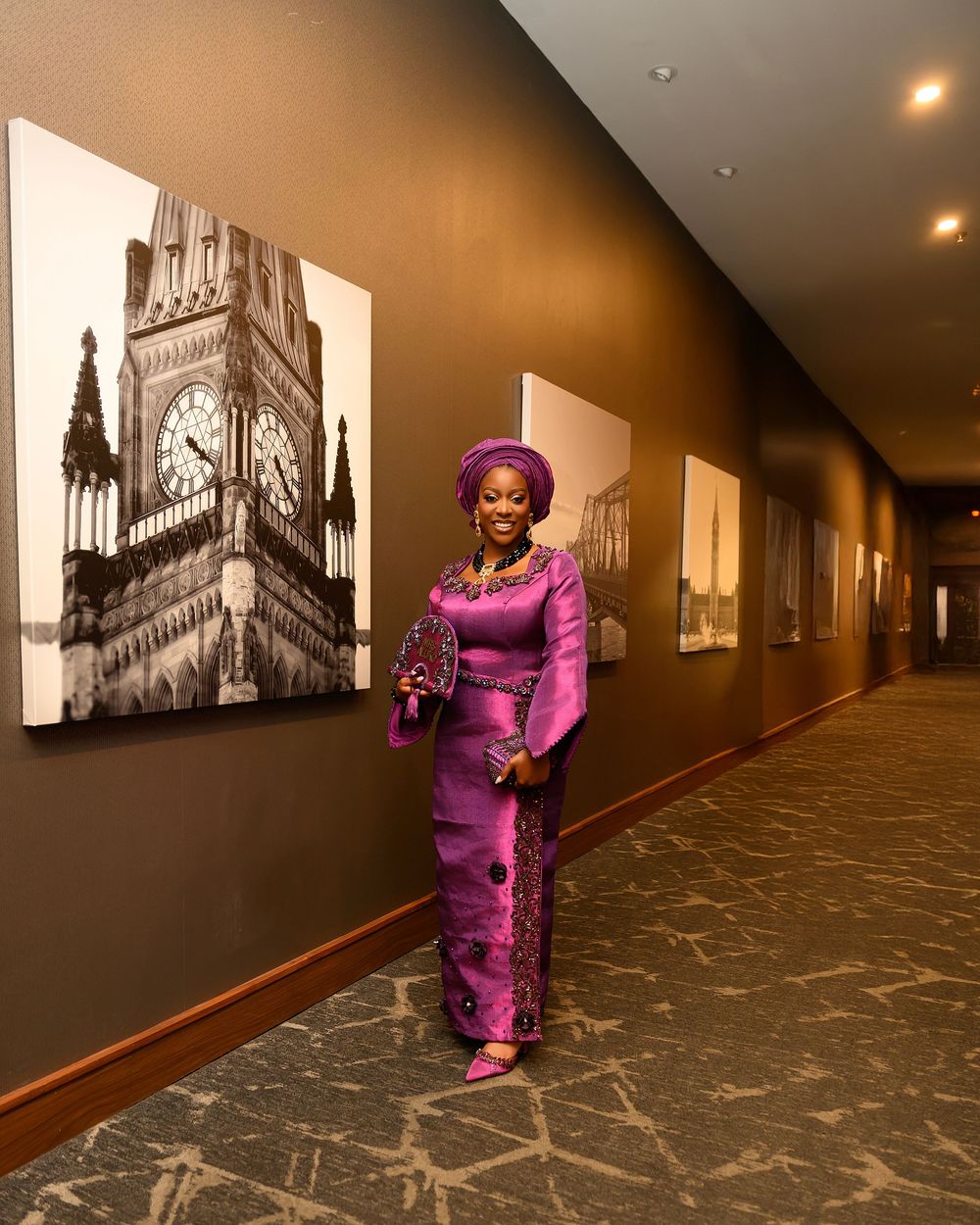 Fisheye view of a long corridor with black and white architectural photos on walls and person in bright purple outfit.