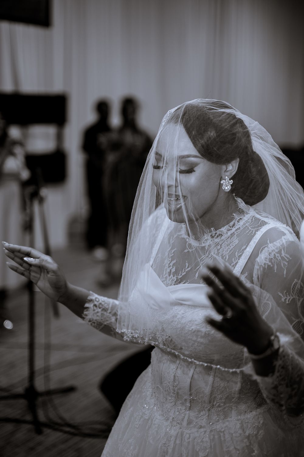 A black and white artistic photograph shows a bride in a flowing veil and dress with outstretched arms in motion.