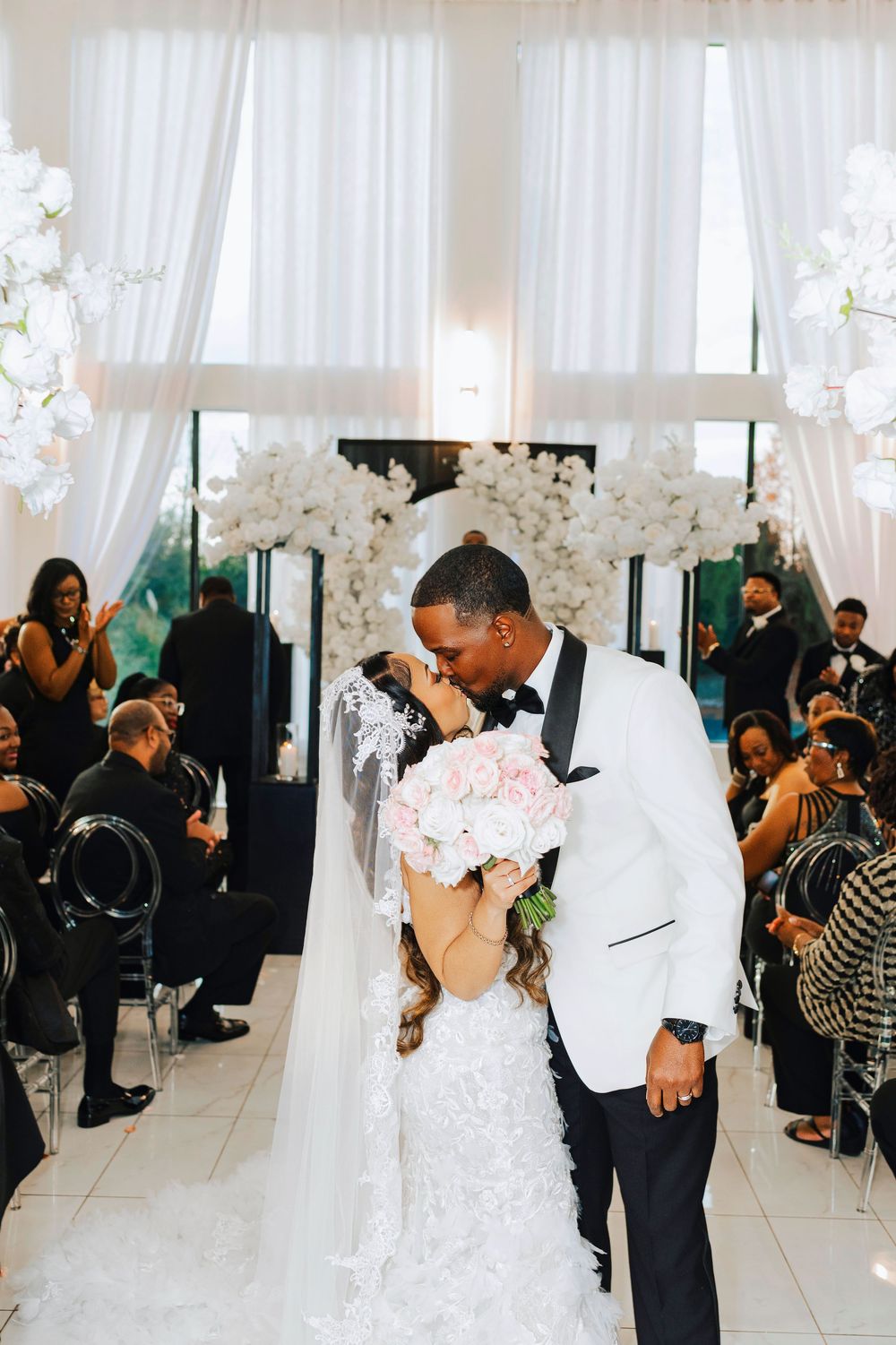A couple shares their first dance at an elegant wedding reception with white decor and guests watching from their seats.