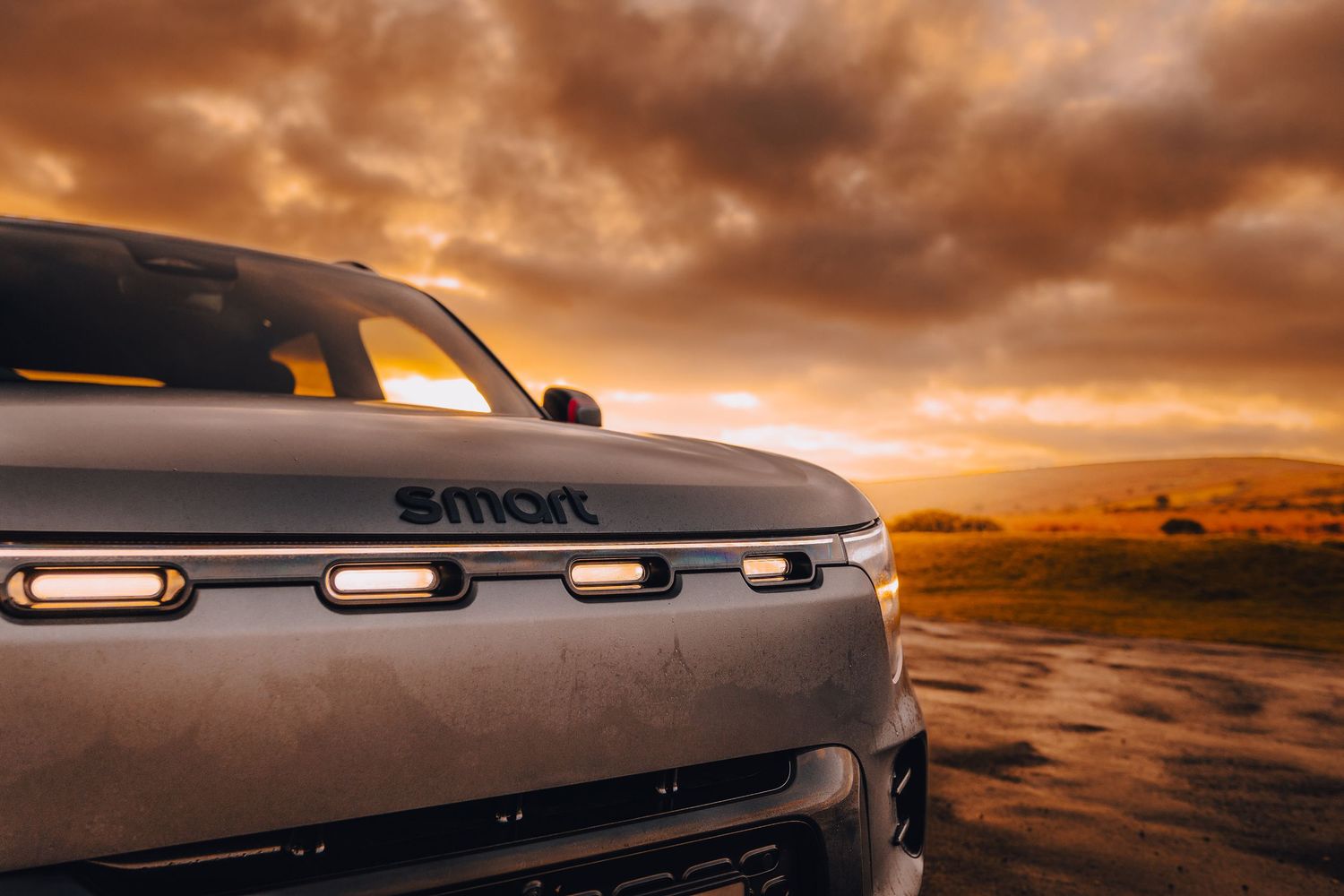 A classic Dodge Challenger drives along a desert road under a dramatic orange sunset sky.