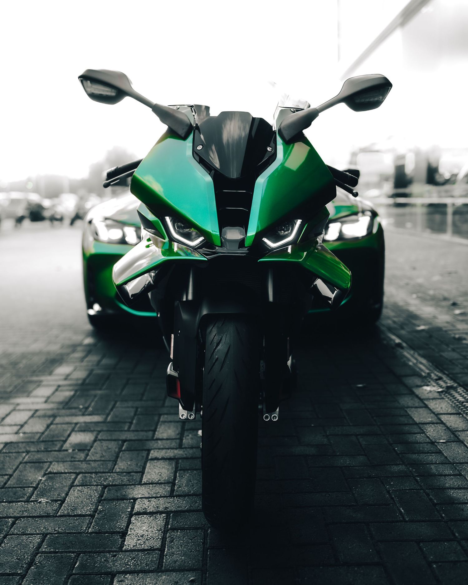 Front view of a sleek green and black sports motorcycle with angular design on cobblestone pavement.