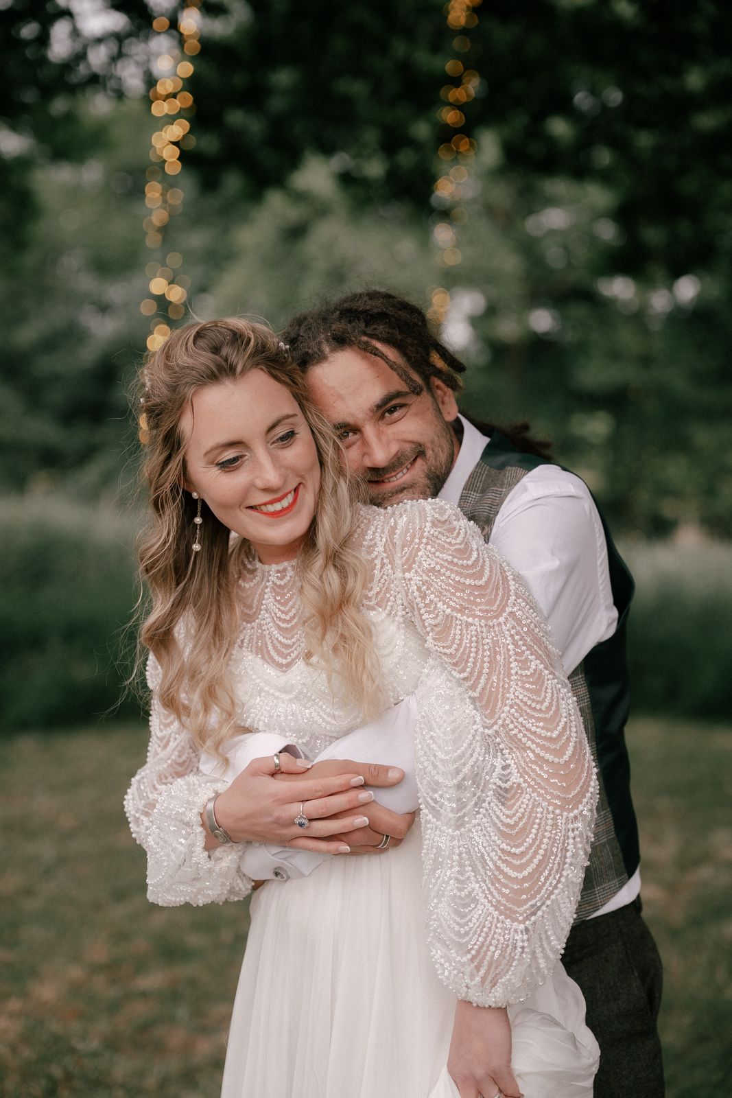 Romantic outdoor couple portrait shows intimate embrace in white lace dress against moody forest backdrop.