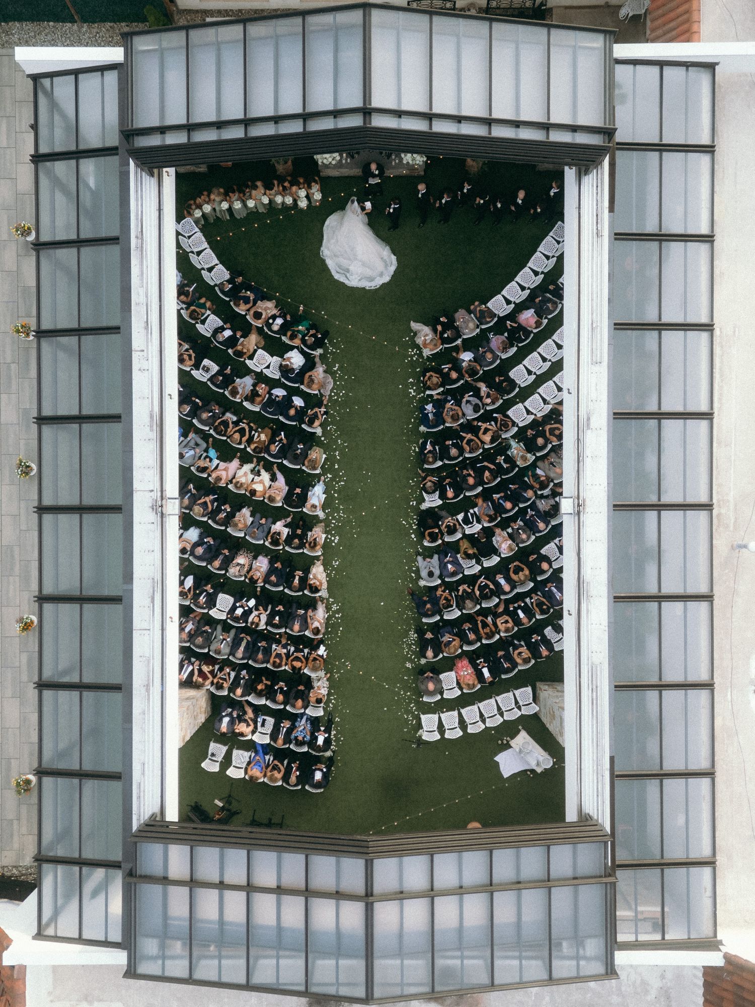 Aerial view of curved rows of chairs arranged in a semi-circular pattern on a green lawn near glass buildings.
