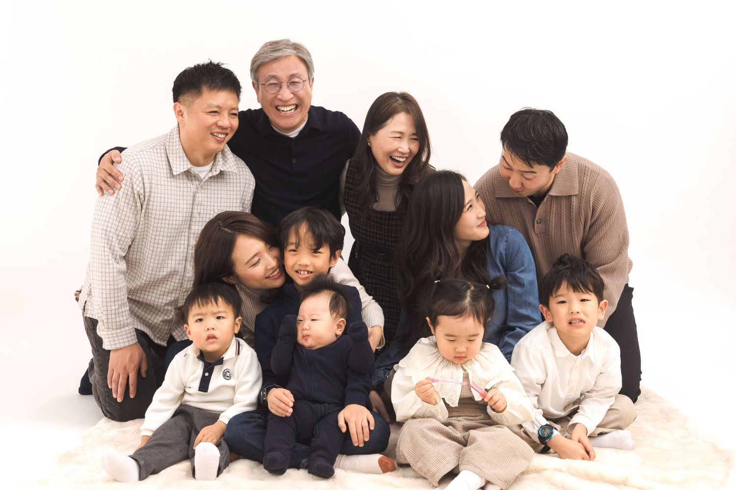 A large family group in coordinated white and navy outfits poses together on a white background for a studio portrait.