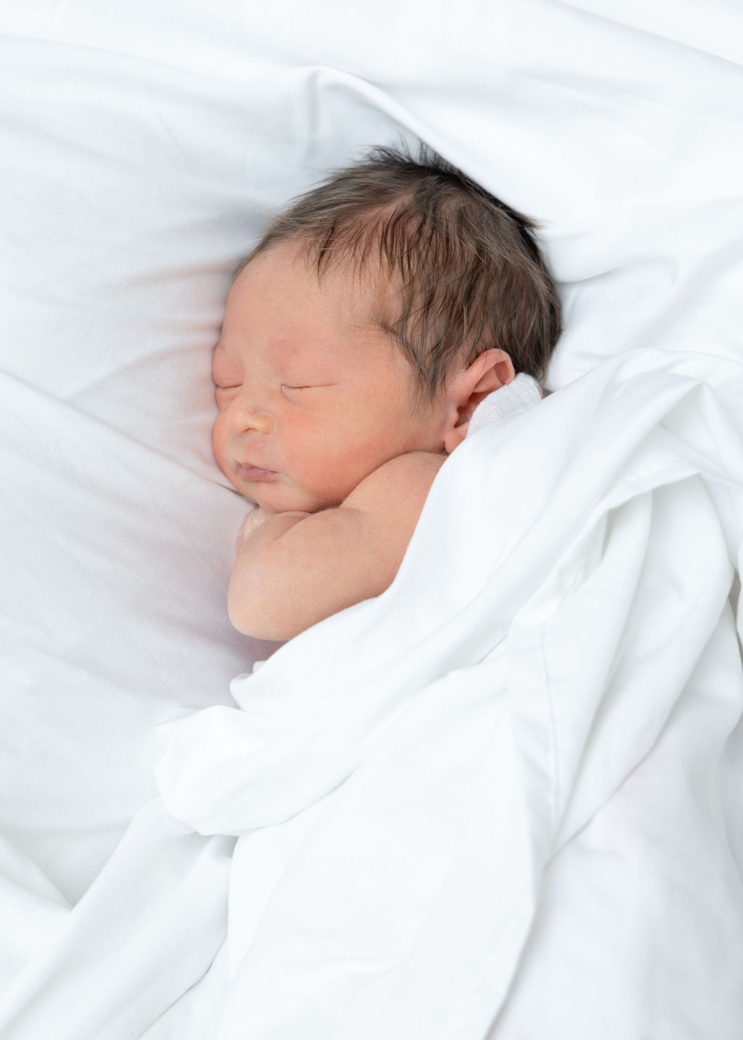 Gentle hands with red nail polish cradle a baby's head showing soft hair.