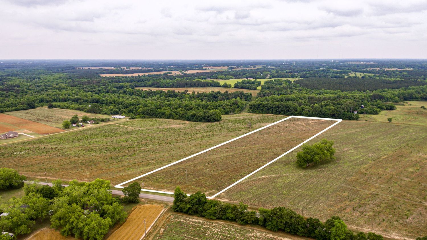 Aerial view of a rural airstrip runway surrounded by farmland and forests stretching into the distance in Cowarts, AL.