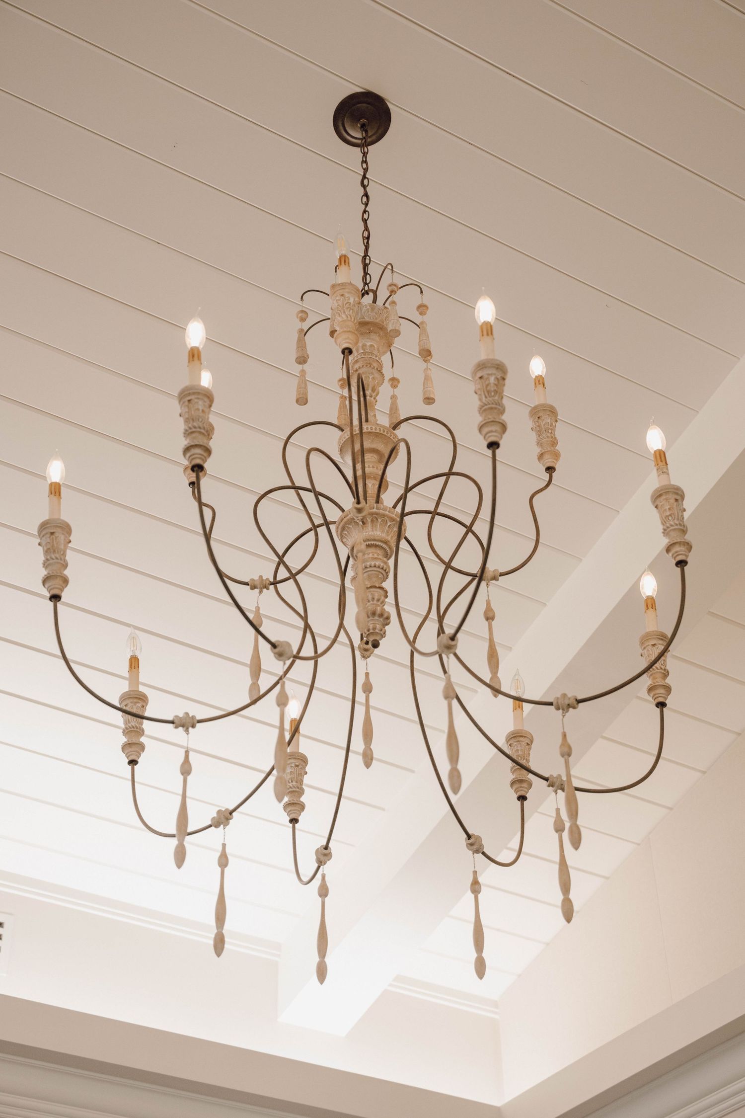 A series of elegant white-washed wooden chandeliers with curved arms and candle-style lights against a white ceiling.
