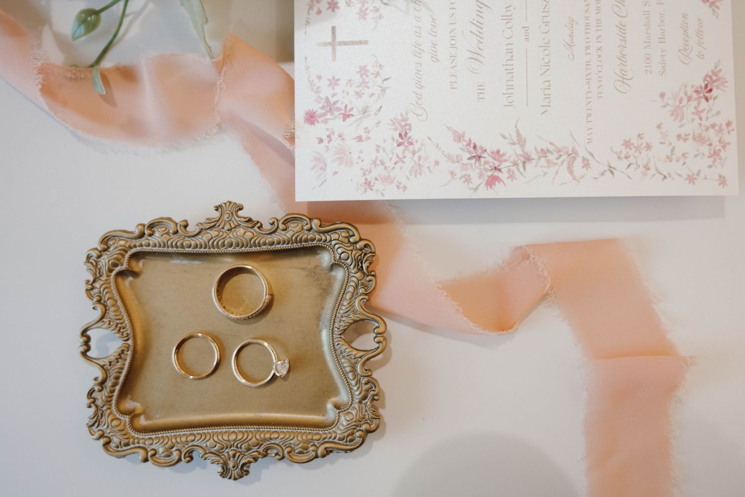 Vintage-style ornate gold frames displaying wedding rings on delicate floral stationery.