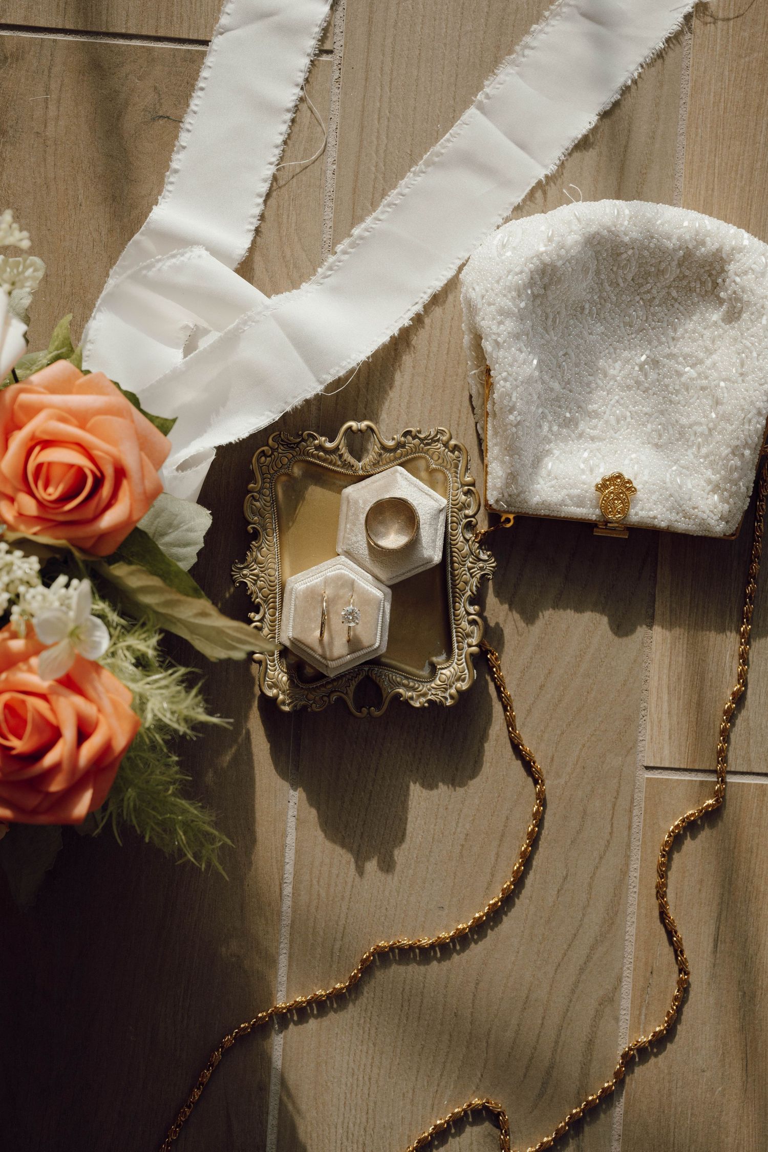 Wedding details including coral roses, white ribbons, and a decorative ring box on wooden surface.