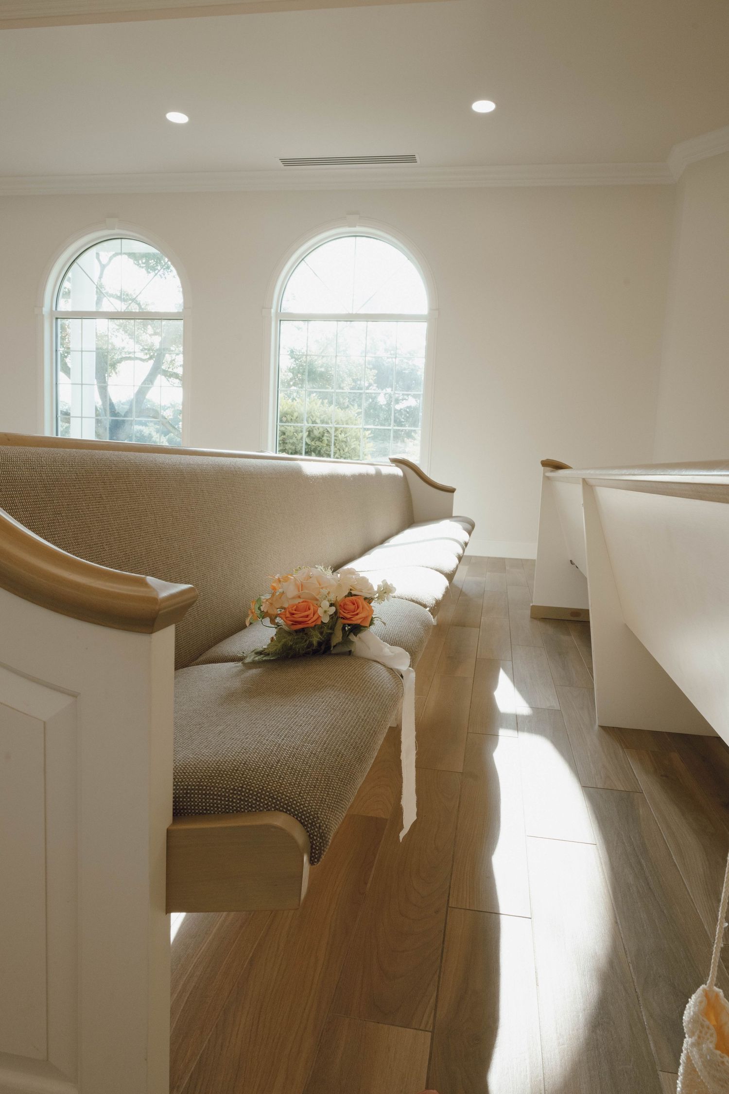 Interior of a modern church or chapel with white walls, arched windows, and wooden pews illuminated by natural light.