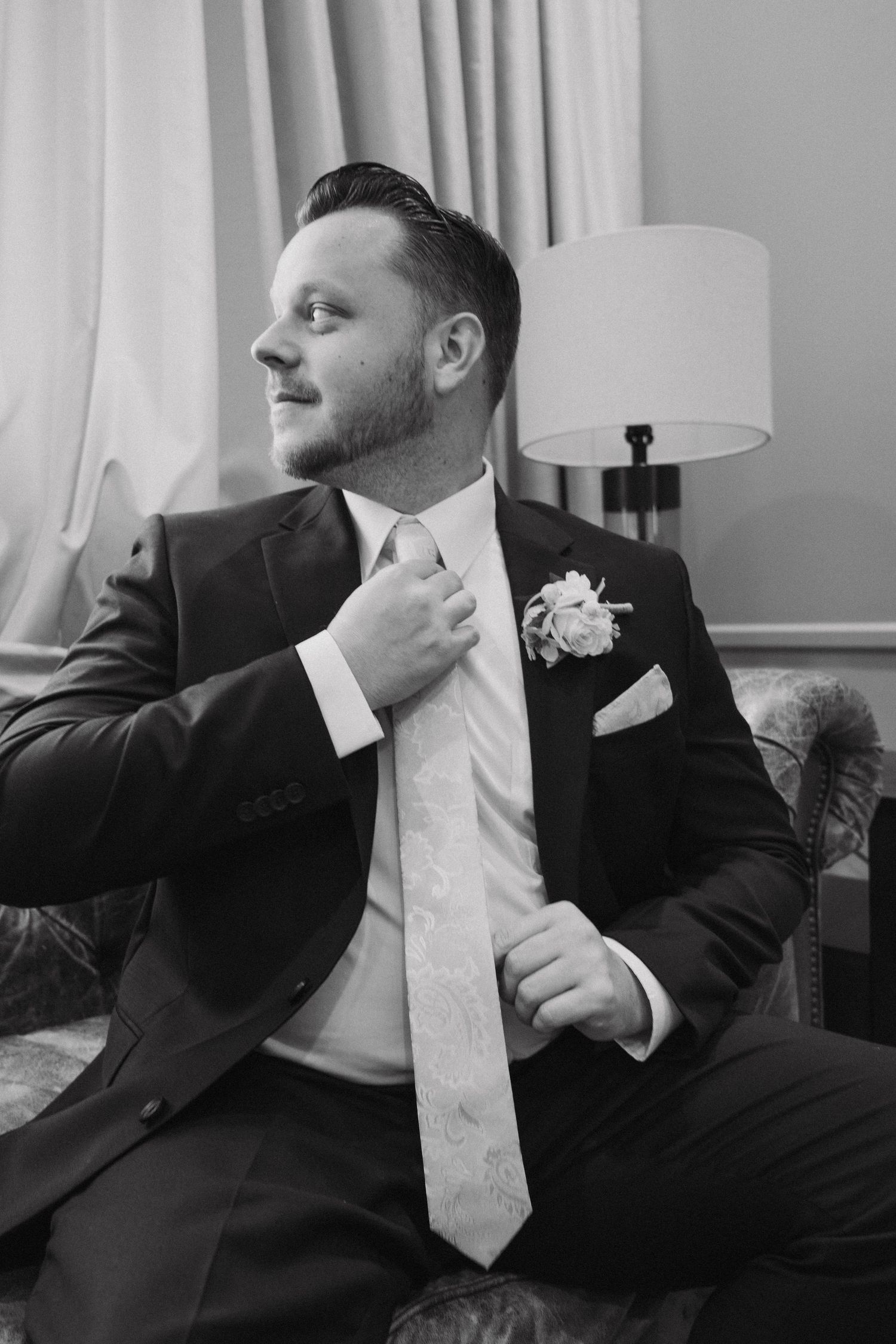 Black and white photo series of a groom in formal attire adjusting his tie and preparing for the wedding day.