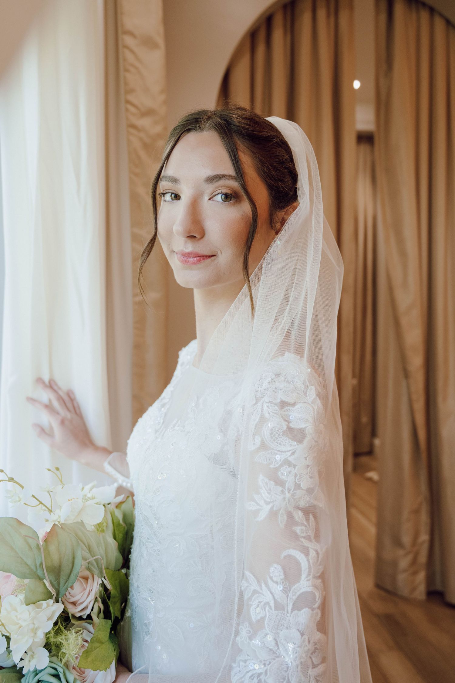 Romantic bridal portraits in soft lighting showcasing delicate lace veil and white floral bouquet details.