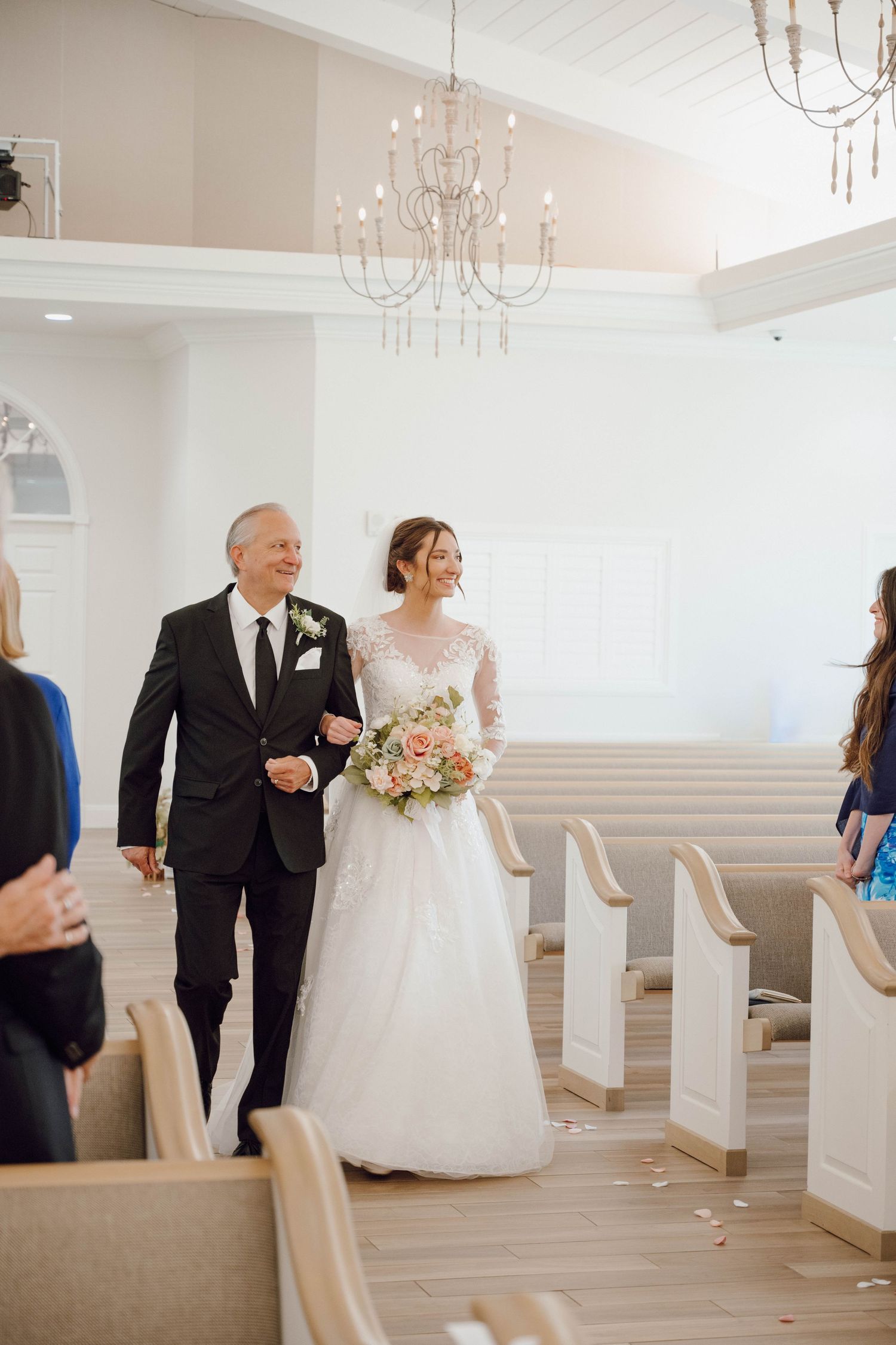 Elegant wedding venue interior with chandelier and wedding party in formal attire.