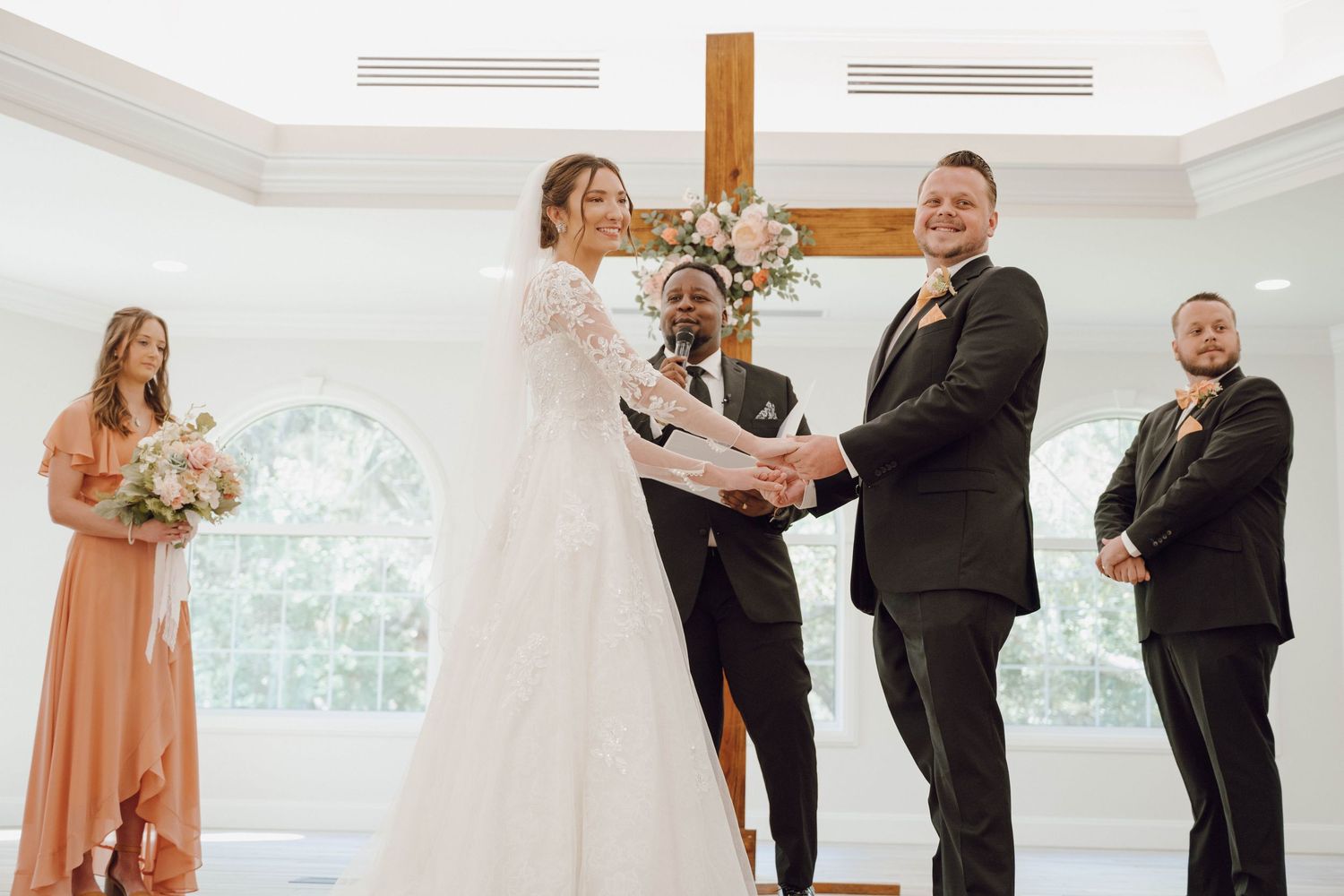 Wedding ceremony taking place in a sunlit chapel with attendants watching the exchange of vows.