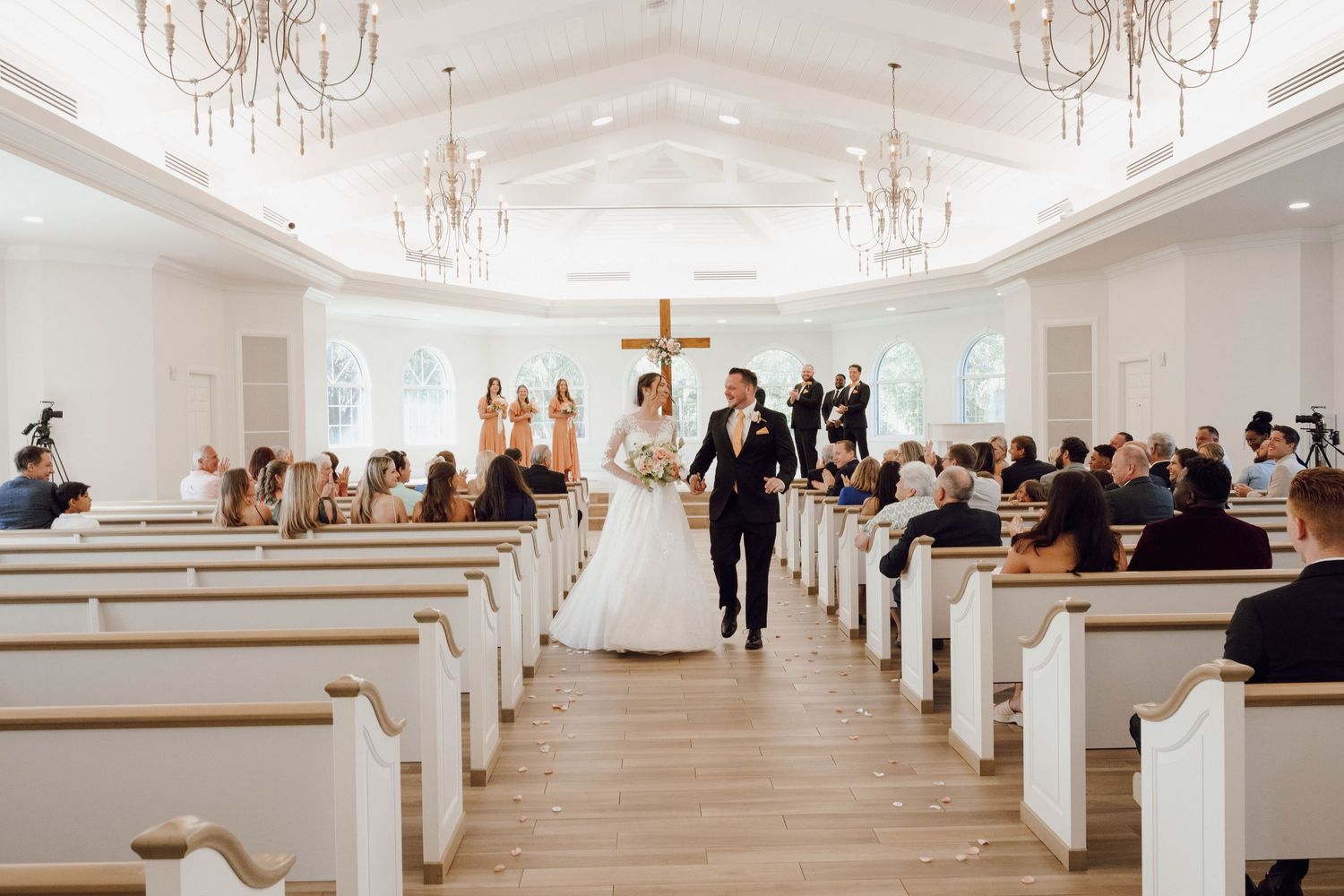 Wide view of a traditional white church interior with pews filled with wedding guests.