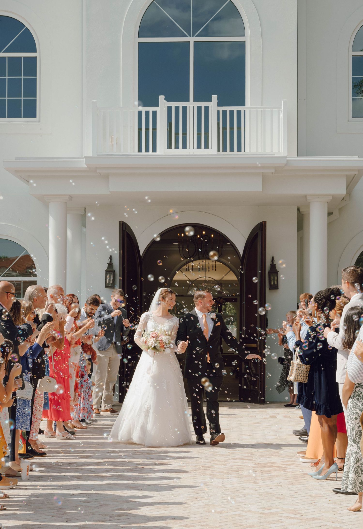 Wedding guests throw confetti at the newlyweds outside a grand white church entrance.