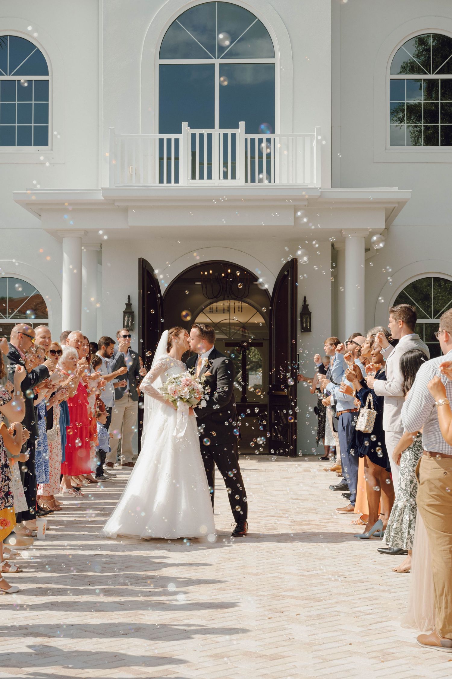 Wedding exit with guests throwing confetti outside an elegant white building with arched windows.