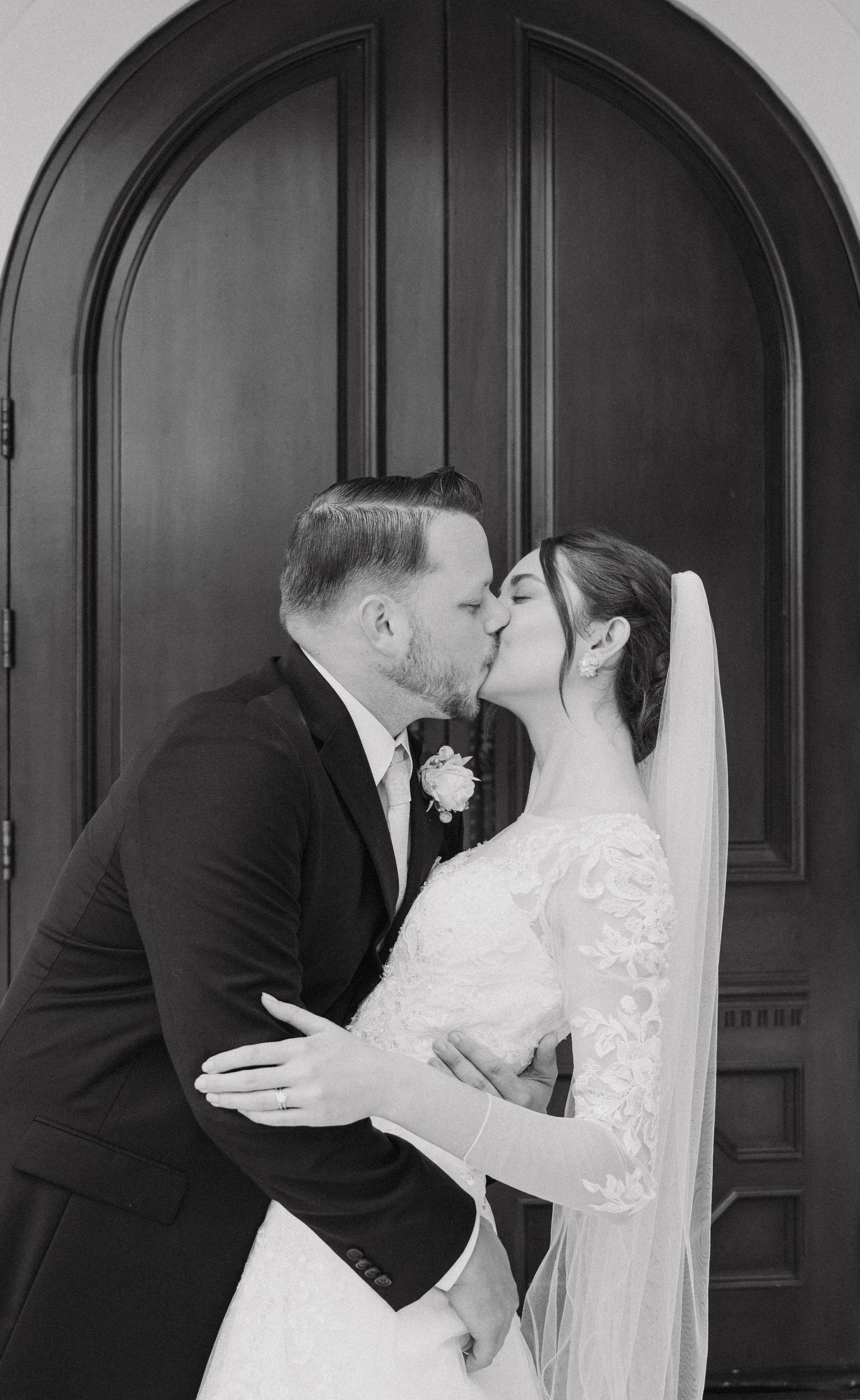 Black and white intimate wedding portrait taken in front of a classic arched wooden door.